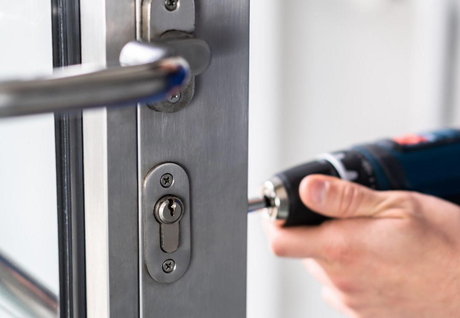 Person uses a power drill to install a silver door lock.