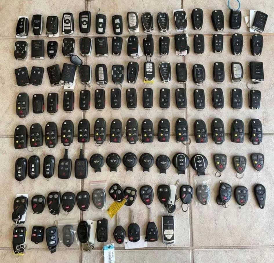 A large collection of car key fobs laid out on a tiled surface.