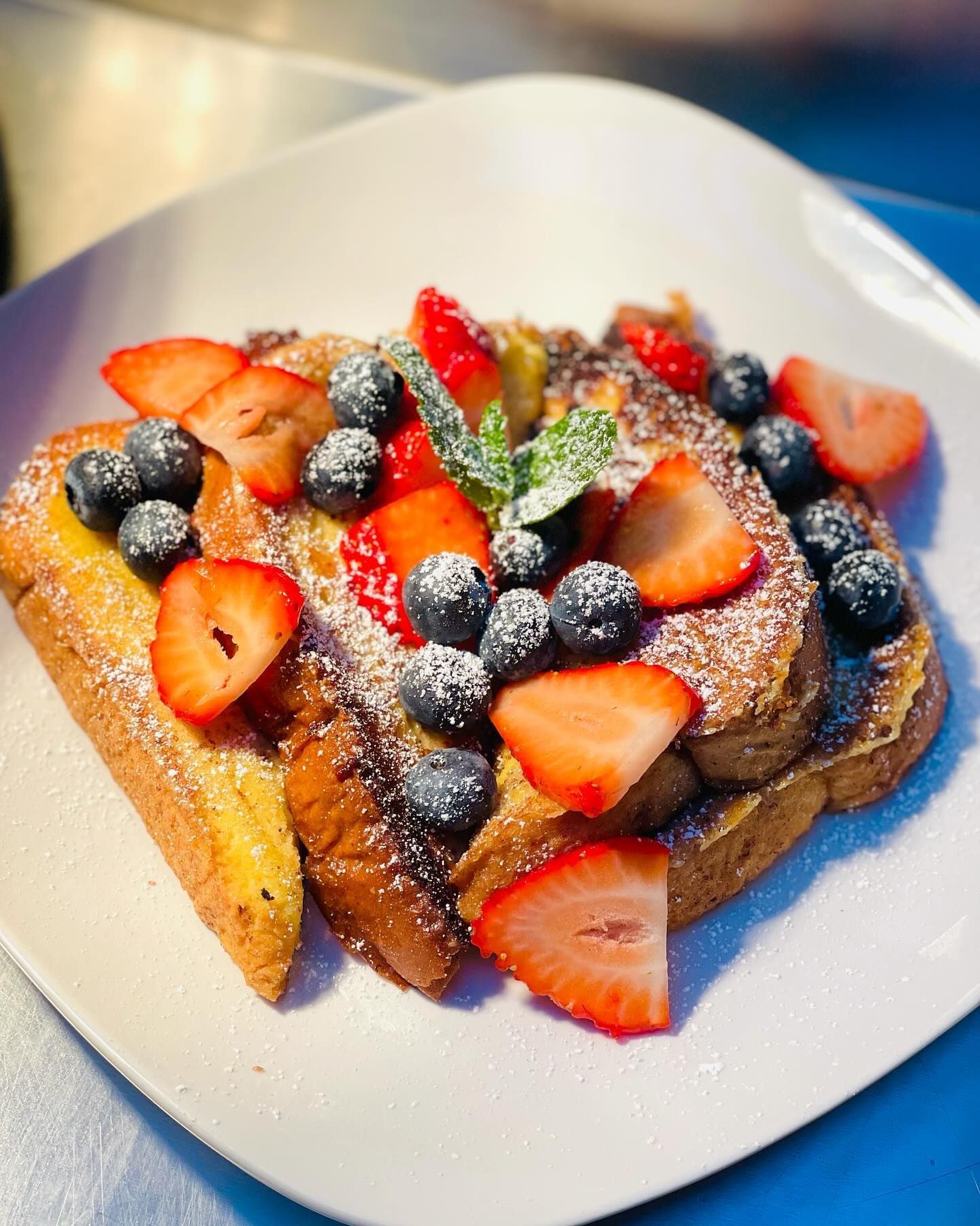 French toast topped with strawberries, blueberries, mint, and powdered sugar on a white plate
