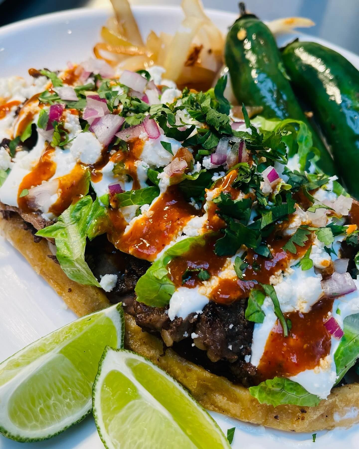 Grilled taco topped with cilantro, onions, crema, and salsa, served with lime wedges and jalapeños