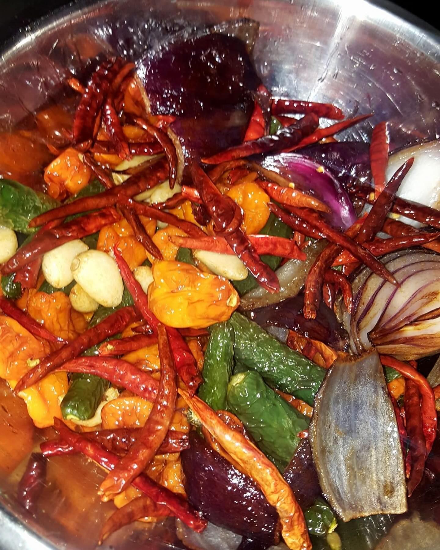 Spicy mixed vegetable dish with red chili peppers, onions, and garlic in a metal bowl