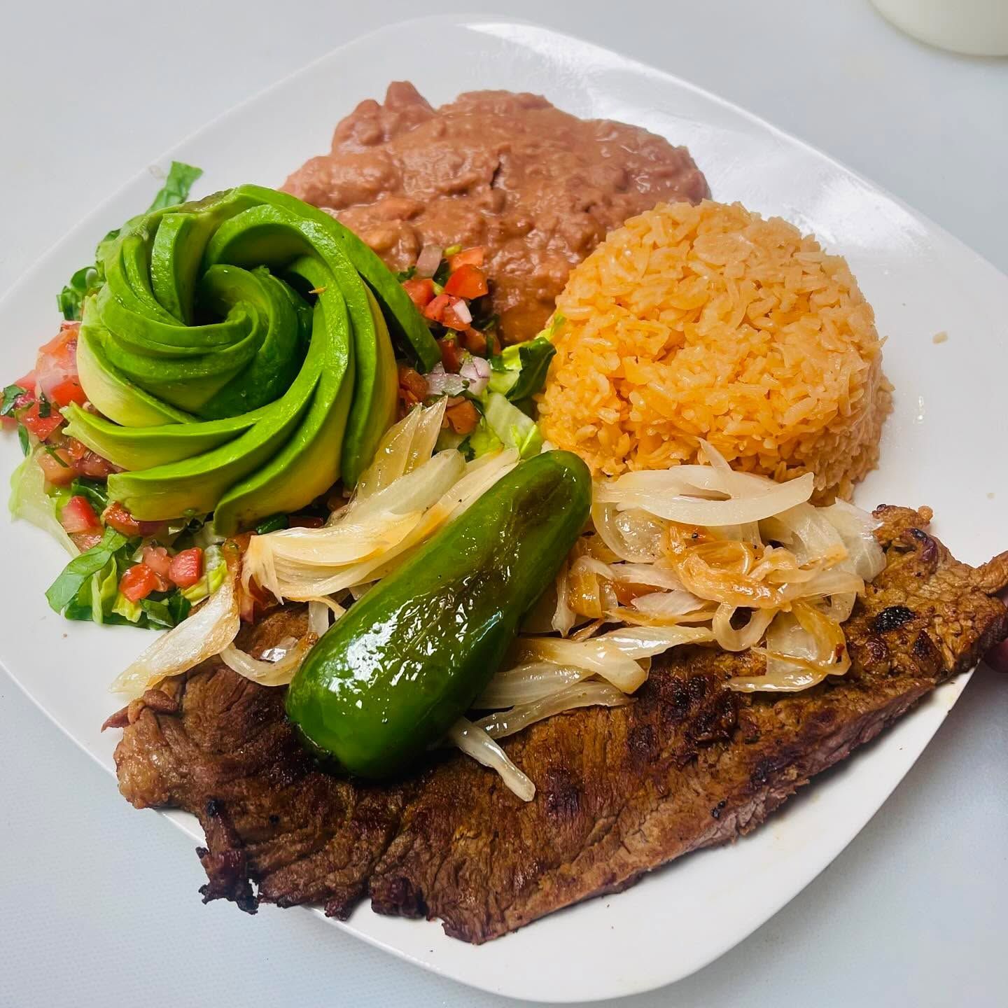 Plate of Mexican food with fish, rice, beans, avocado rose, salsa, and grilled onion