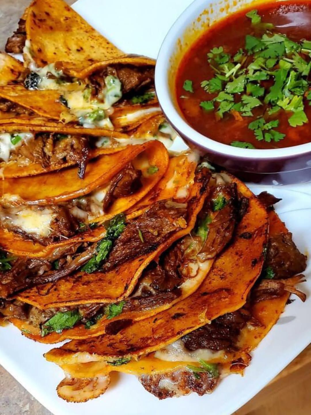 Crispy folded quesadillas on a white plate with red salsa topped with cilantro