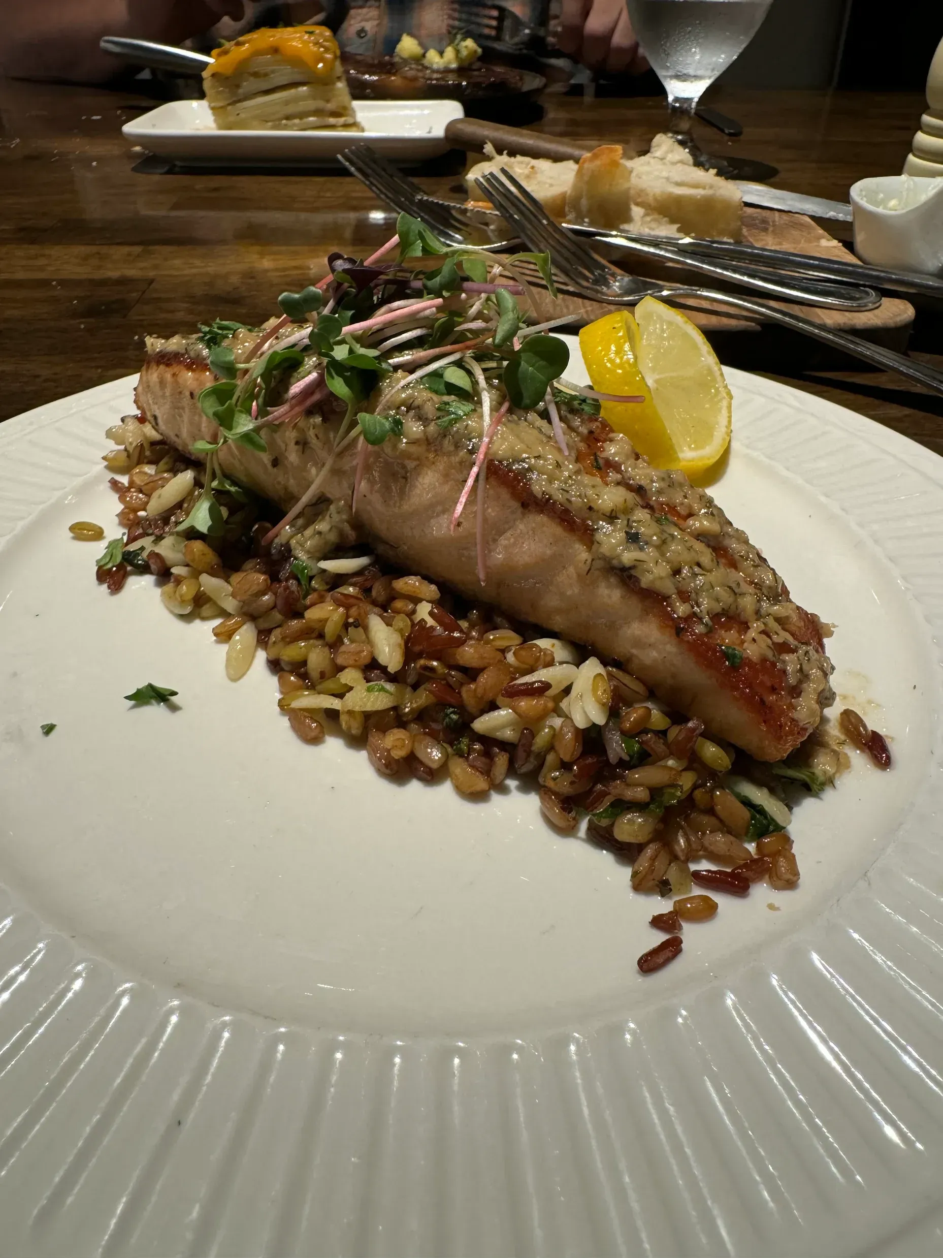 A seared salmon fillet topped with herbs and a lemon wedge, served over a bed of grains on a white plate.