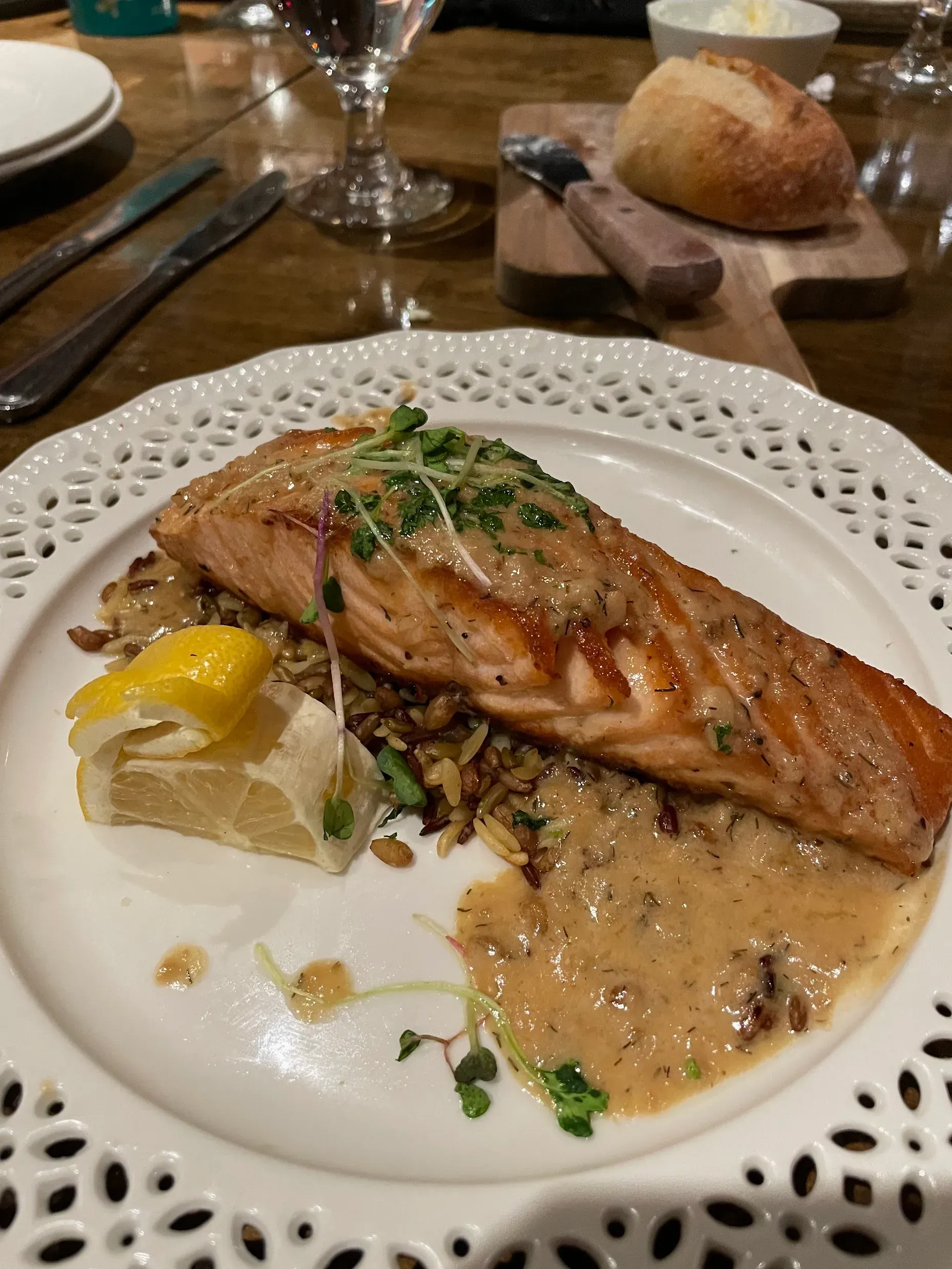 A seared salmon fillet served on wild rice with a creamy sauce and a lemon wedge on a decorative white plate.