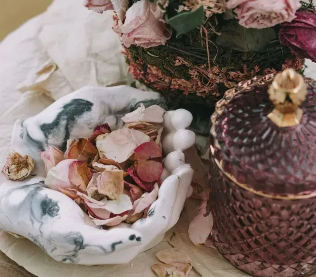 A hands-shaped bowl filled with a fragrant potpourri of flower petals, and a dried floral bouquet.