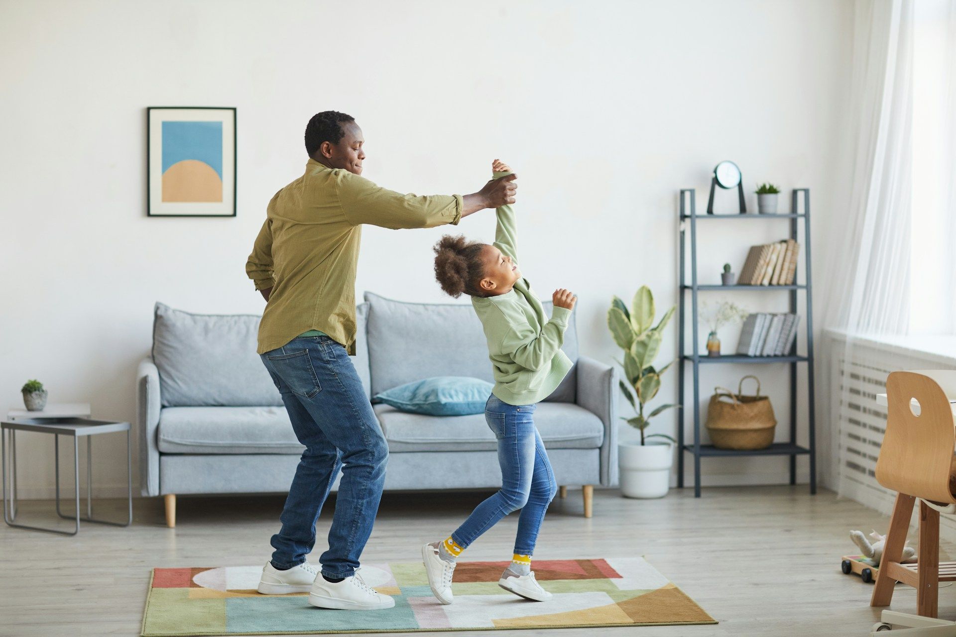 Man and child dancing together in a living room, smiling, with a rug and sofa.