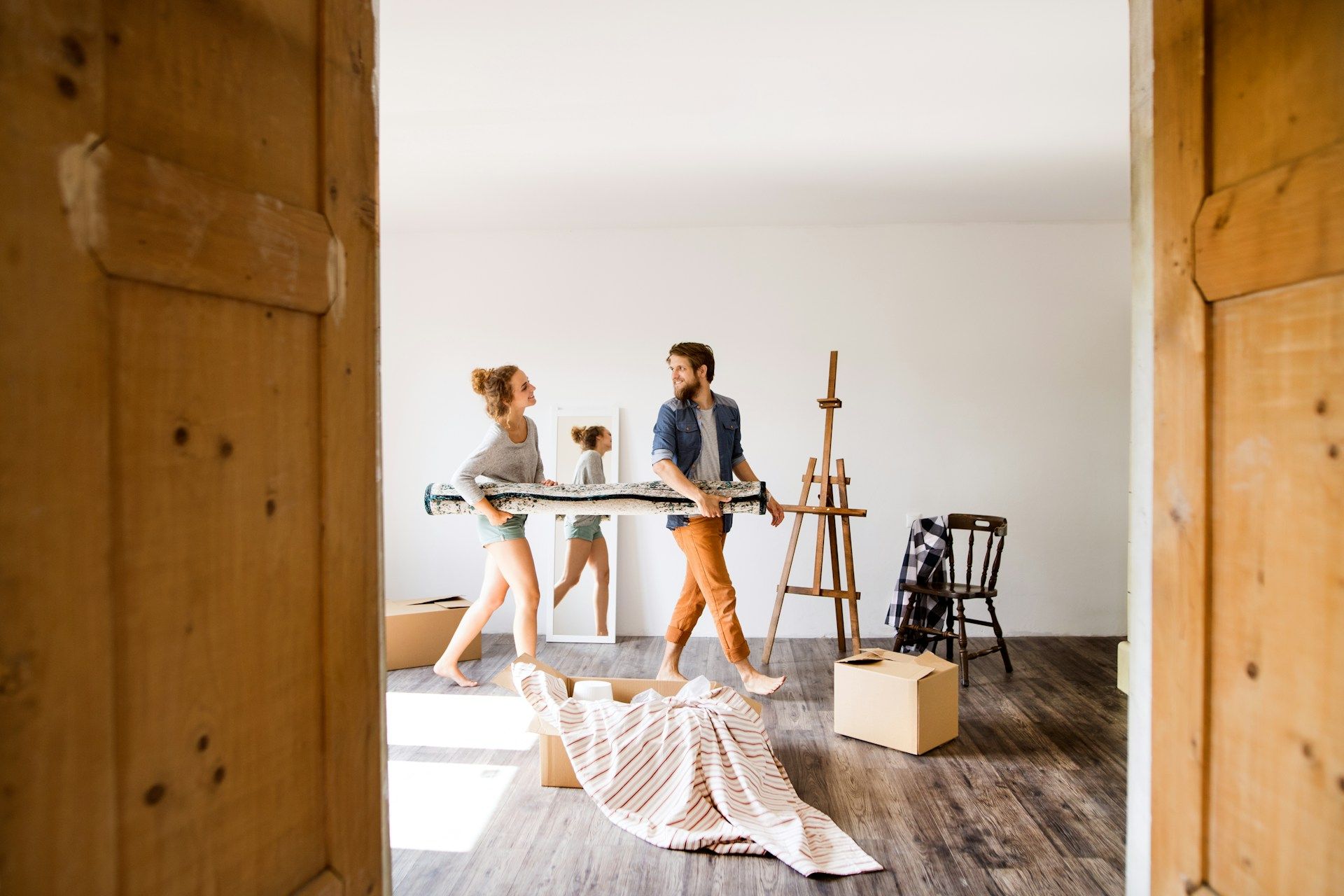 Couple carrying rolled-up painting, mirror, and moving into a new home.