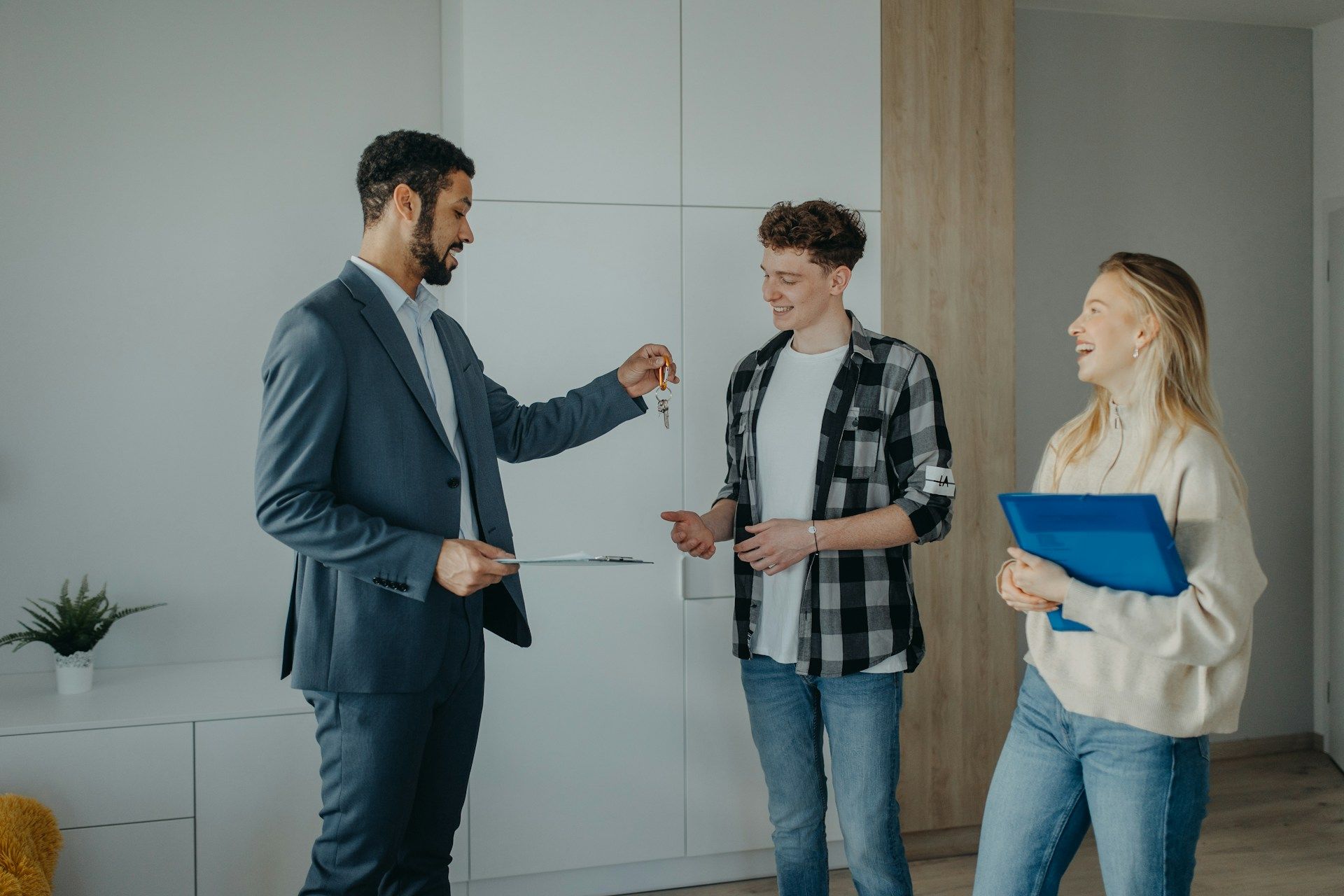 Real estate agent handing keys to a couple in a bright room.