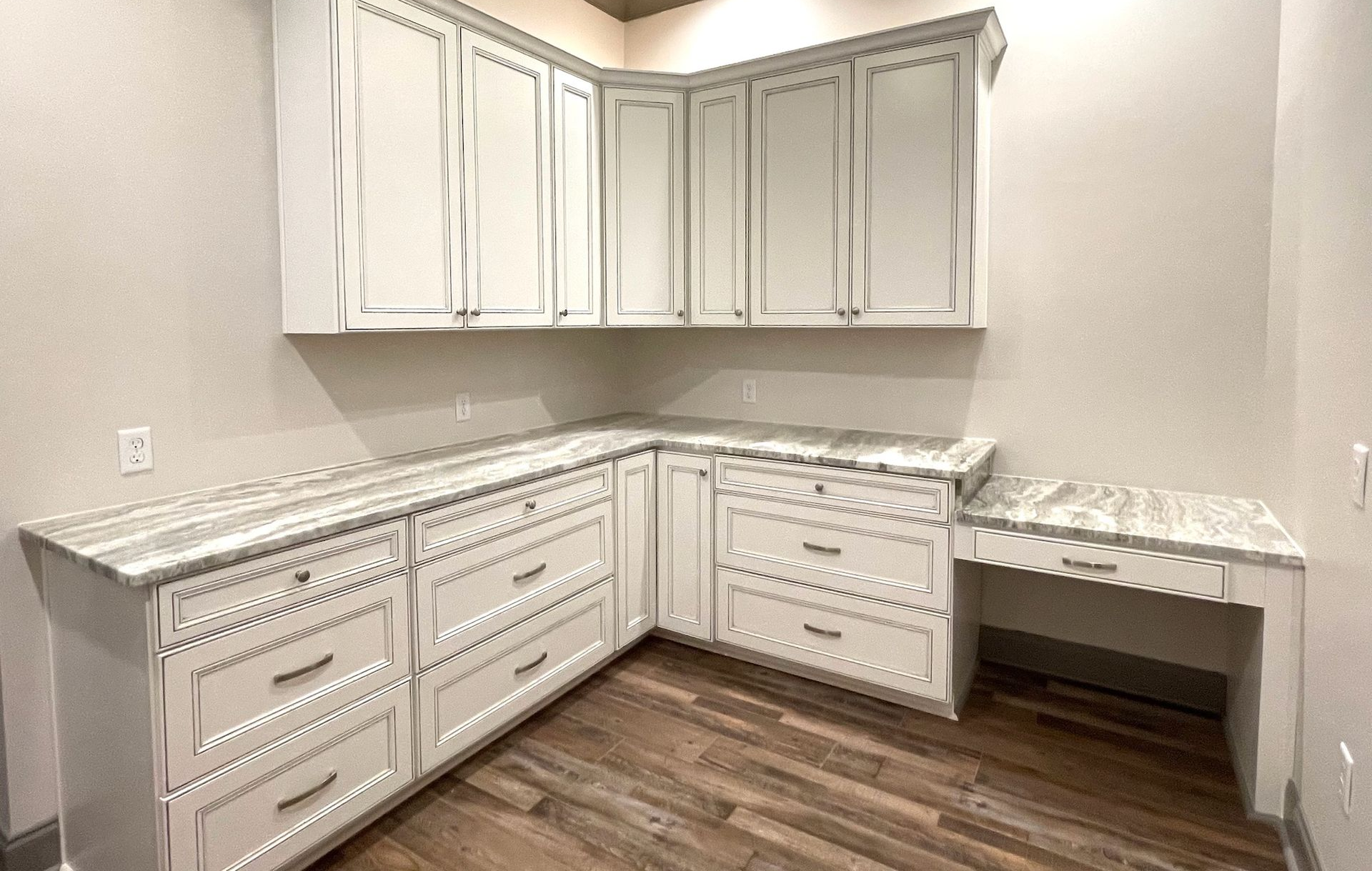 White L-shaped kitchen with marble countertops, upper cabinets, and wood floor in an empty room