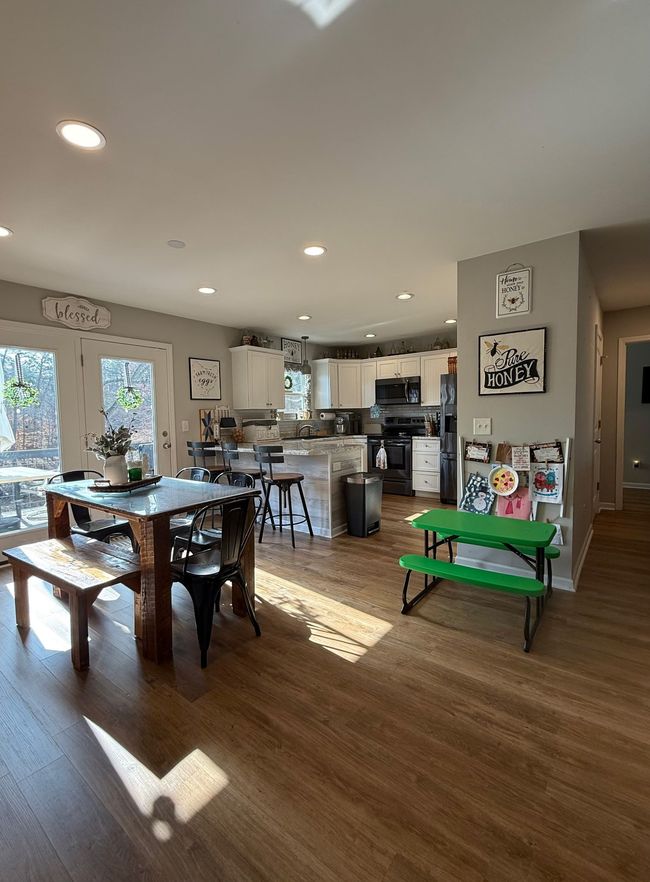 Bright open kitchen and dining area with wood floors, French doors, and a small green bench nearby