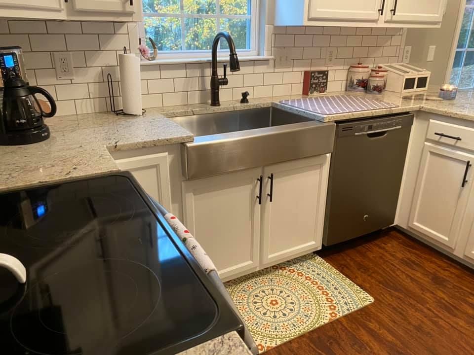Bright kitchen with black stove, stainless sink, dishwasher, and white cabinets under a window