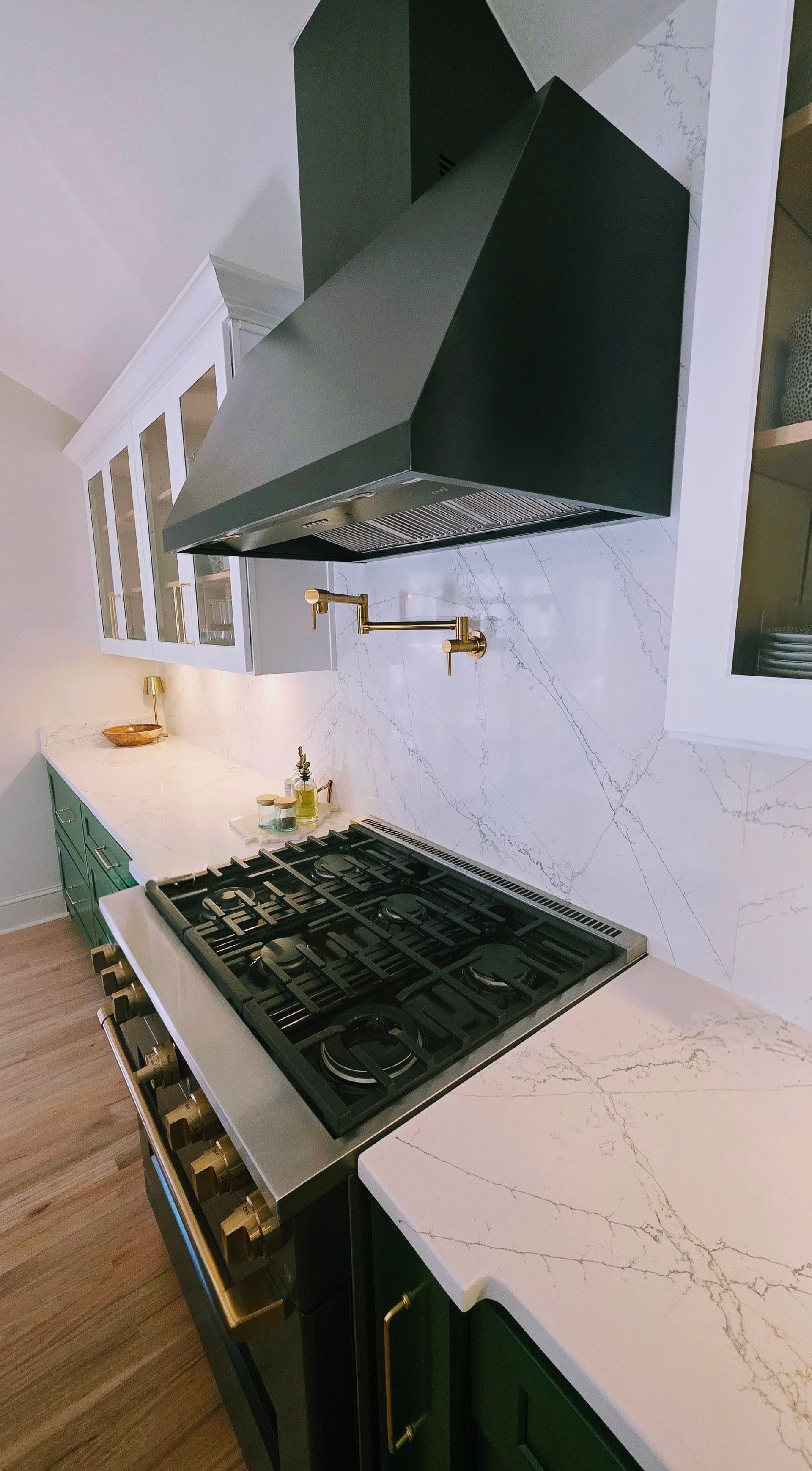 Modern kitchen with green cabinets, white countertops, and black range hood.