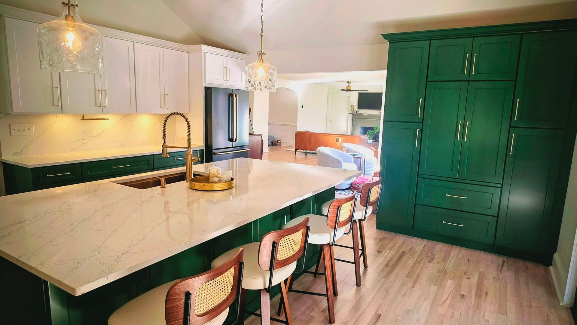 Green and white kitchen with island, wooden stools, and large green cabinets.