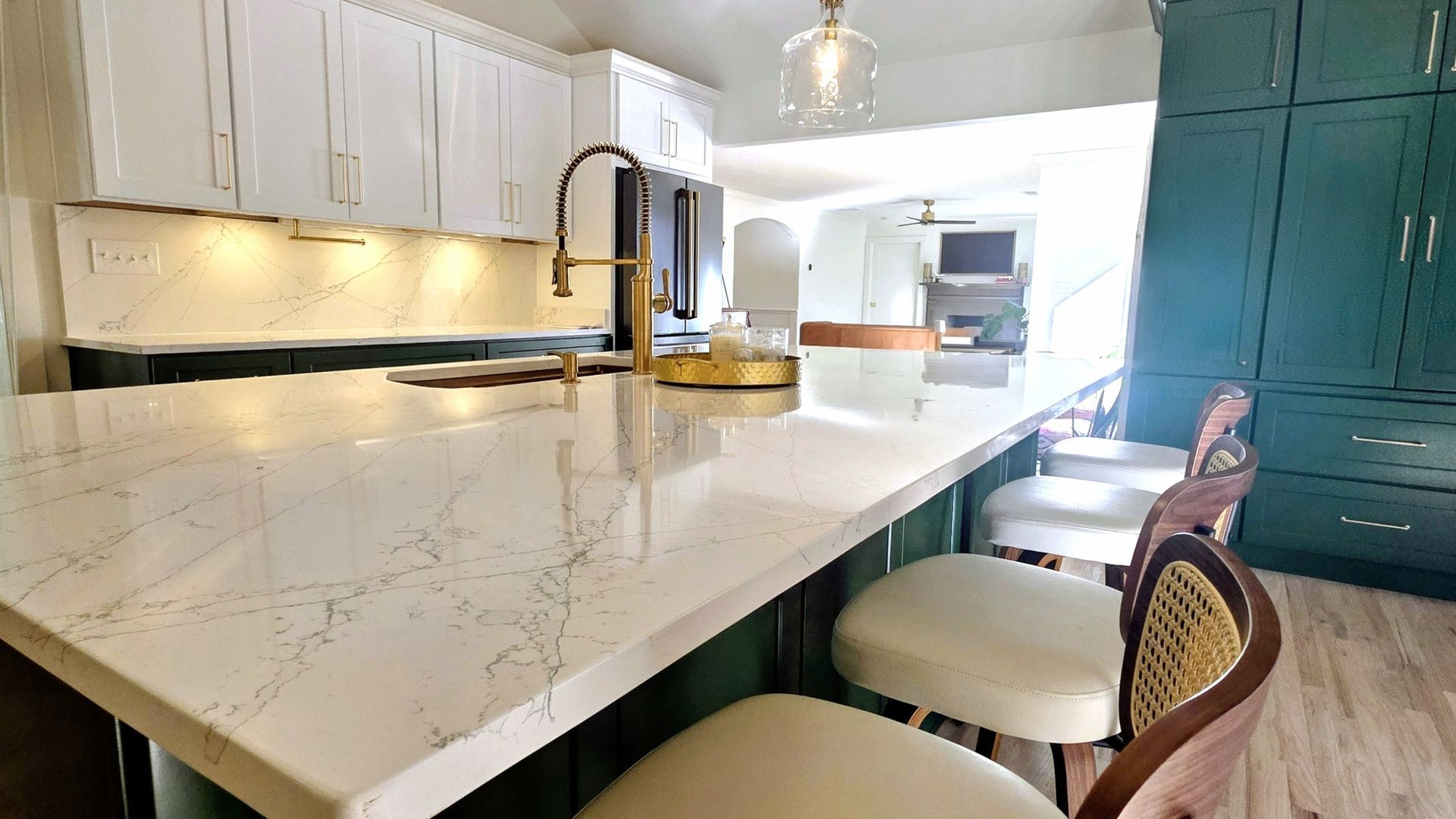 Modern kitchen with white countertops and teal cabinets. Gold faucet and bar stools.