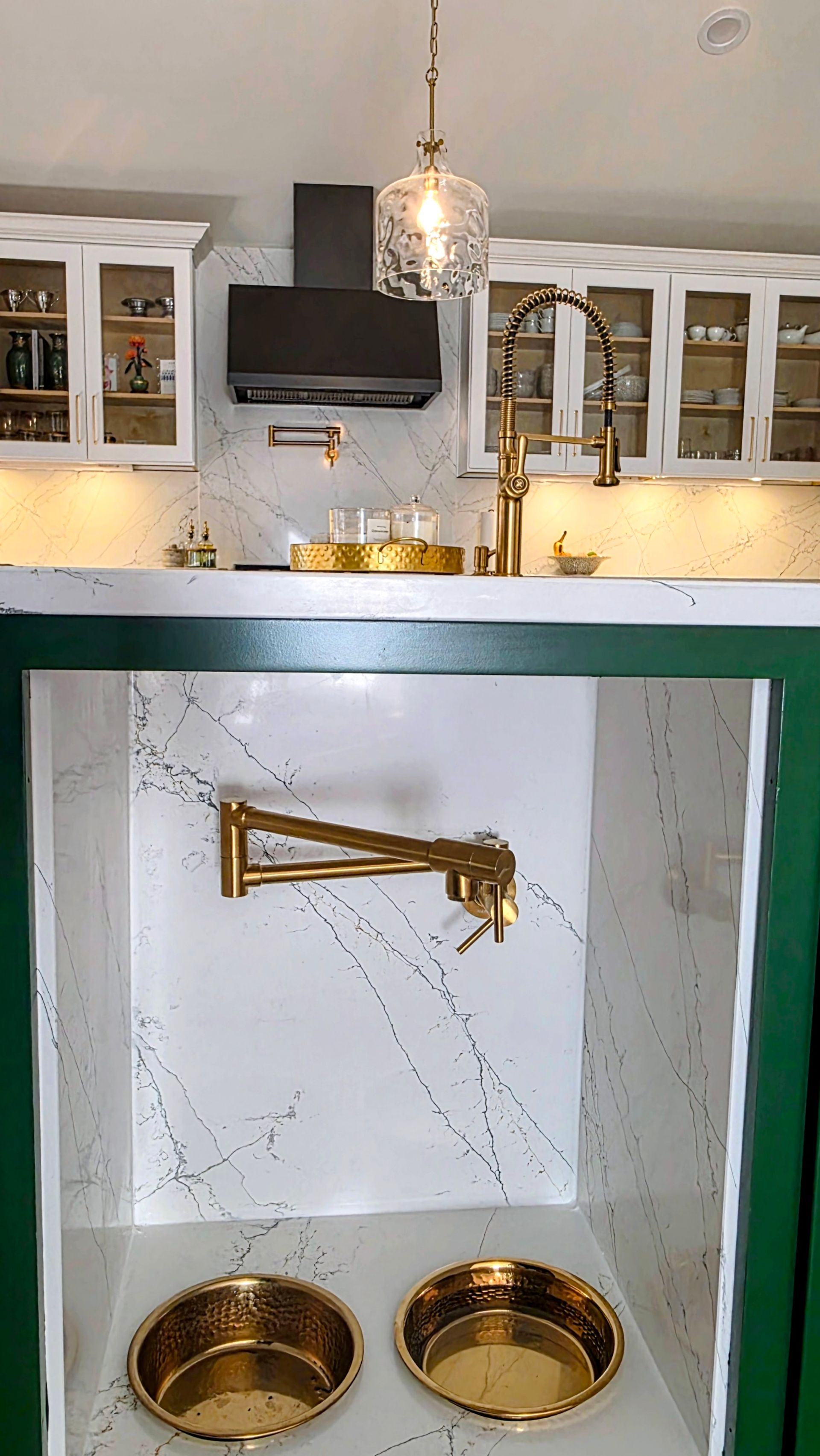 Gold pot filler above two gold dog bowls in a white and green kitchen.