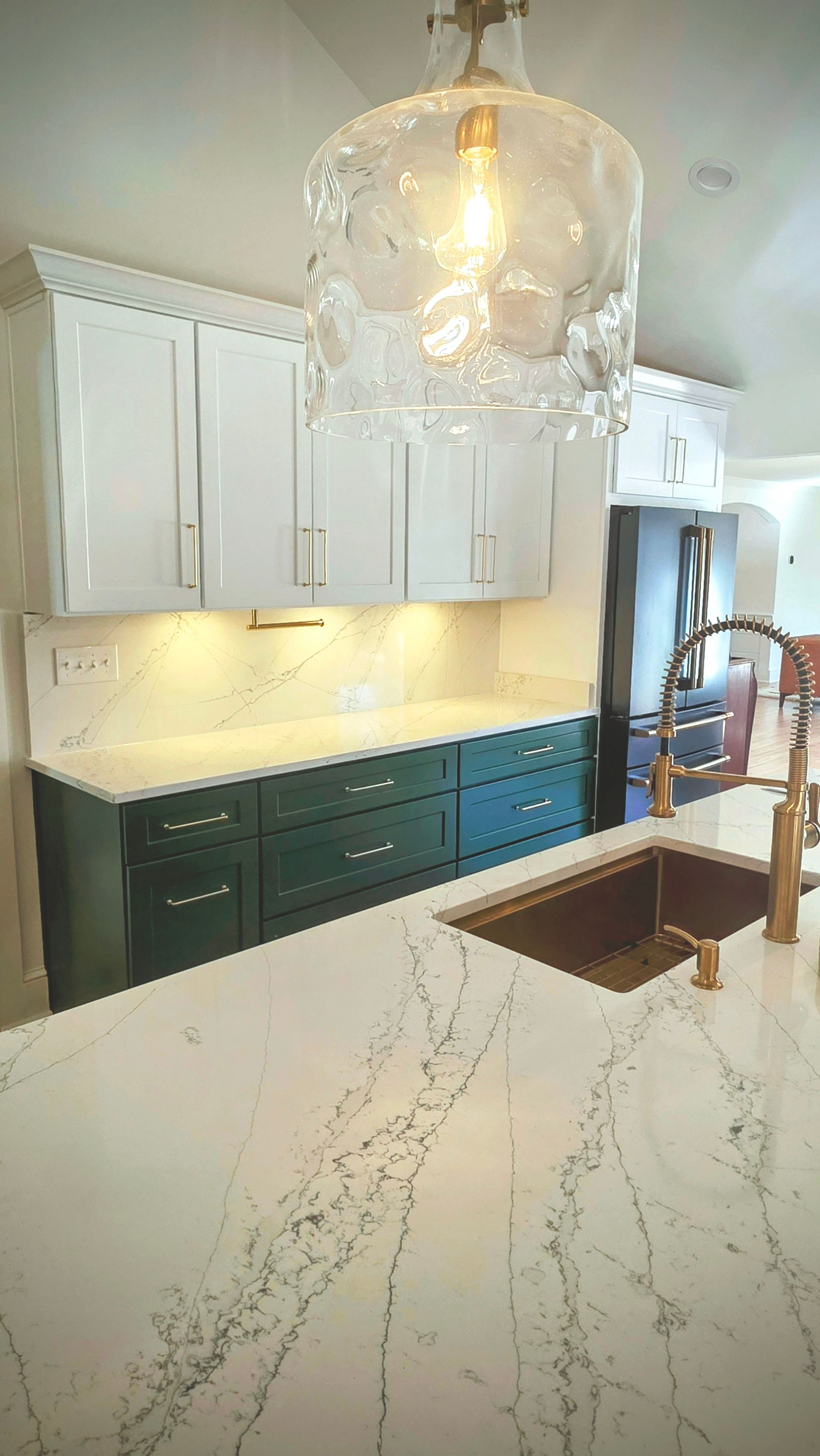 Kitchen with white and teal cabinets, marble countertop, gold faucet, and a decorative glass light fixture.
