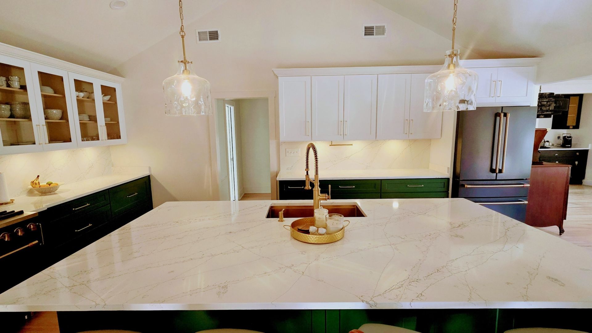 Modern kitchen with white and green cabinets, gold fixtures, and large island with speckled countertop.