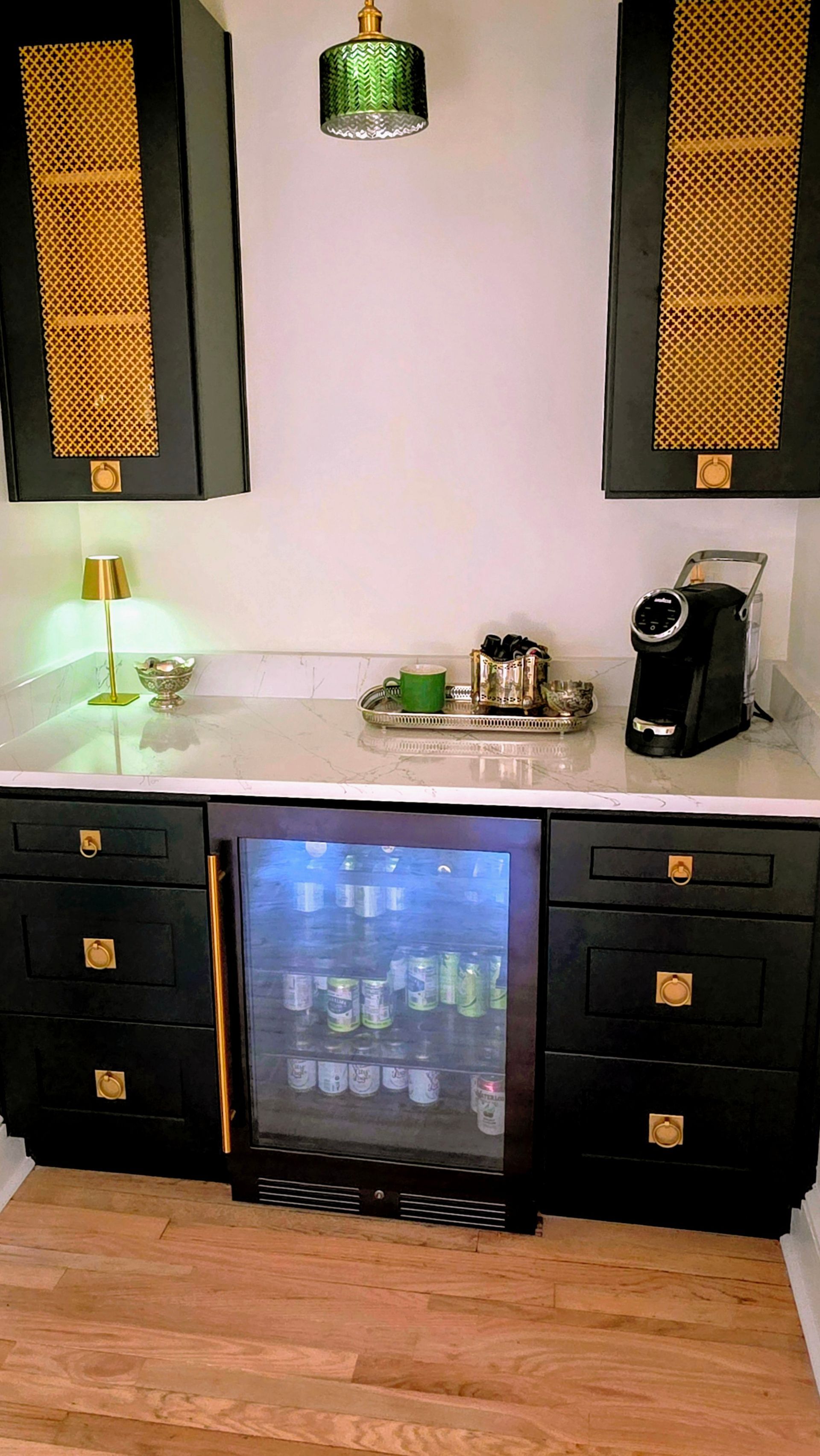 Black cabinets with gold hardware, a wine fridge, and a coffee machine in a kitchen setting.