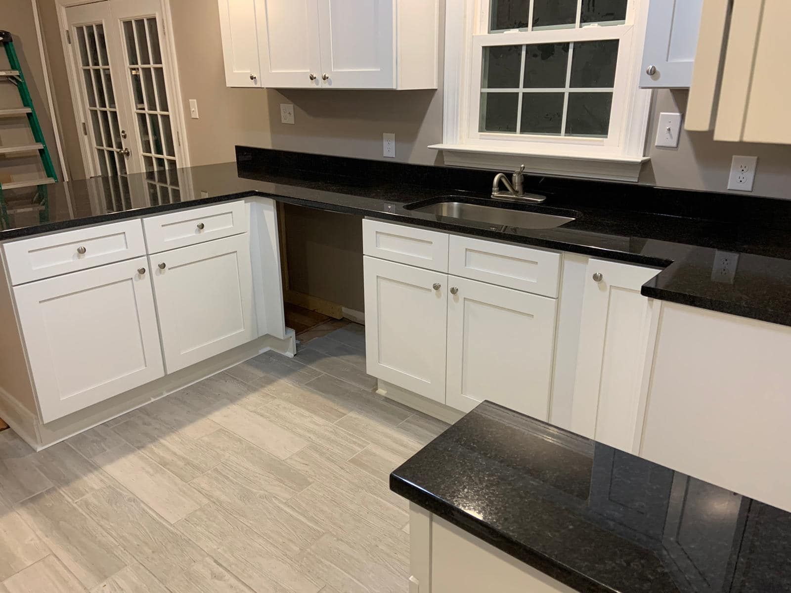 Empty kitchen with white cabinets, black countertops, and a peninsula under renovation.
