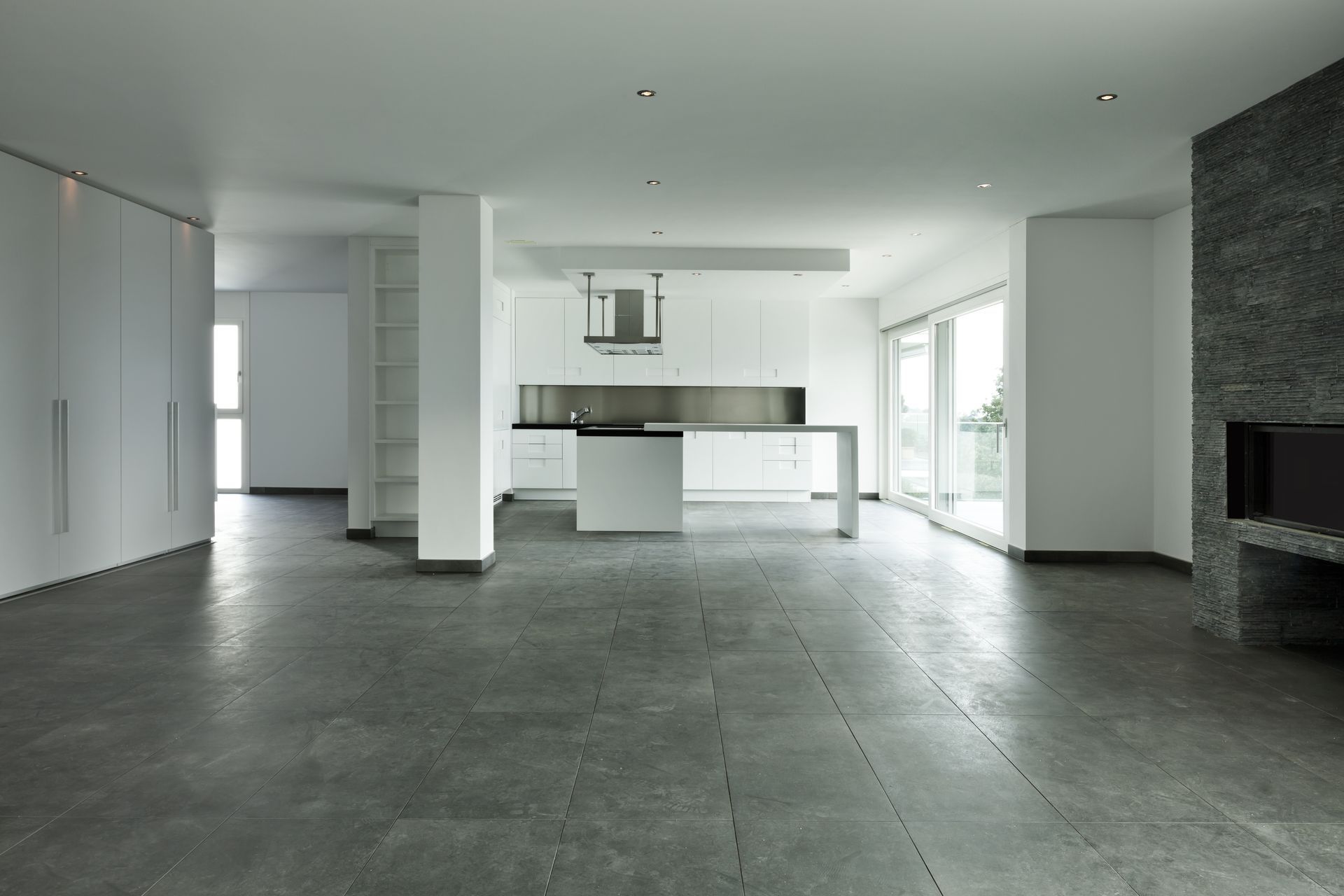 Empty modern open-plan kitchen and living area with gray tile floors and white walls