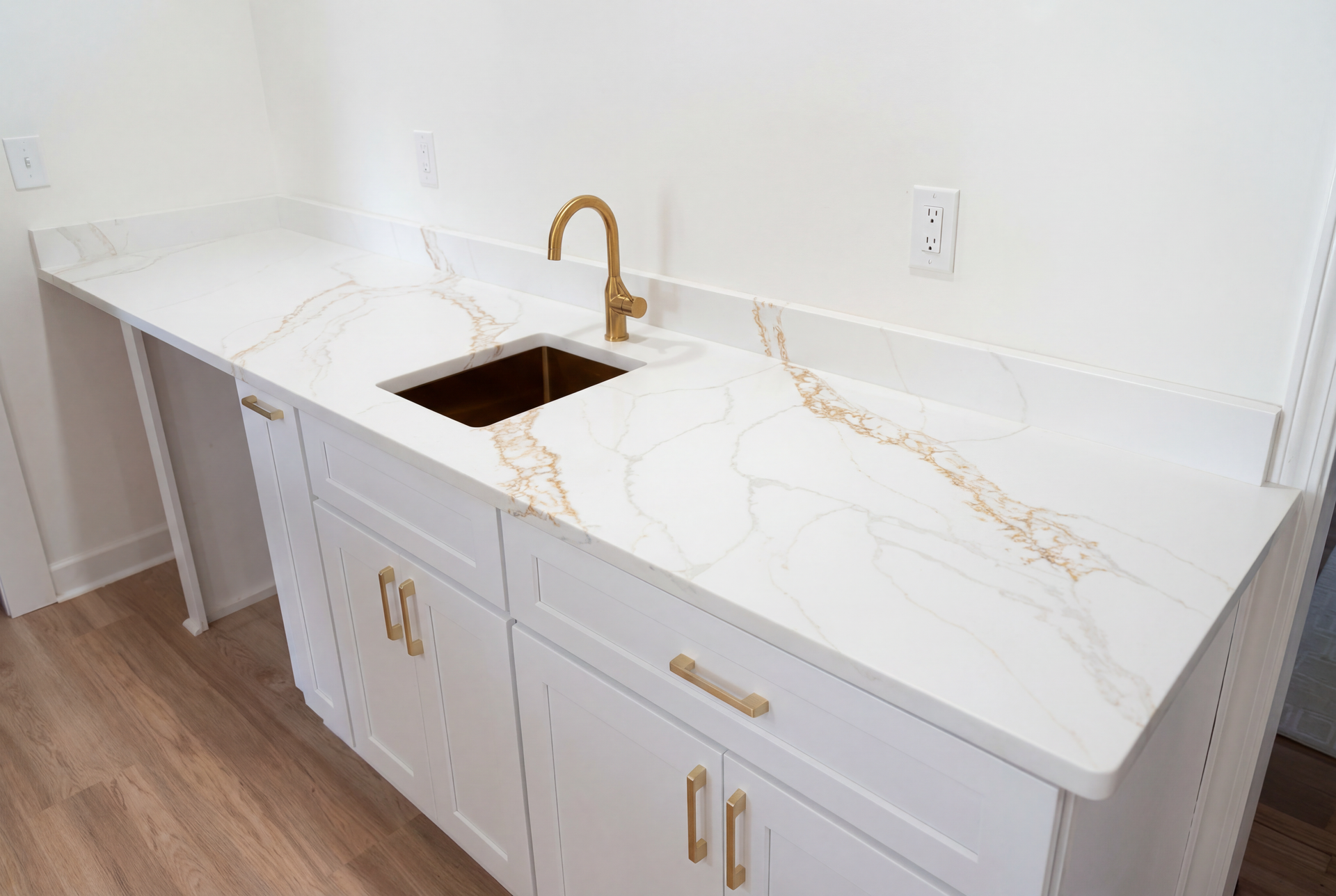 White cabinets with gold hardware and a sink, topped with a marble countertop, and a gold faucet.