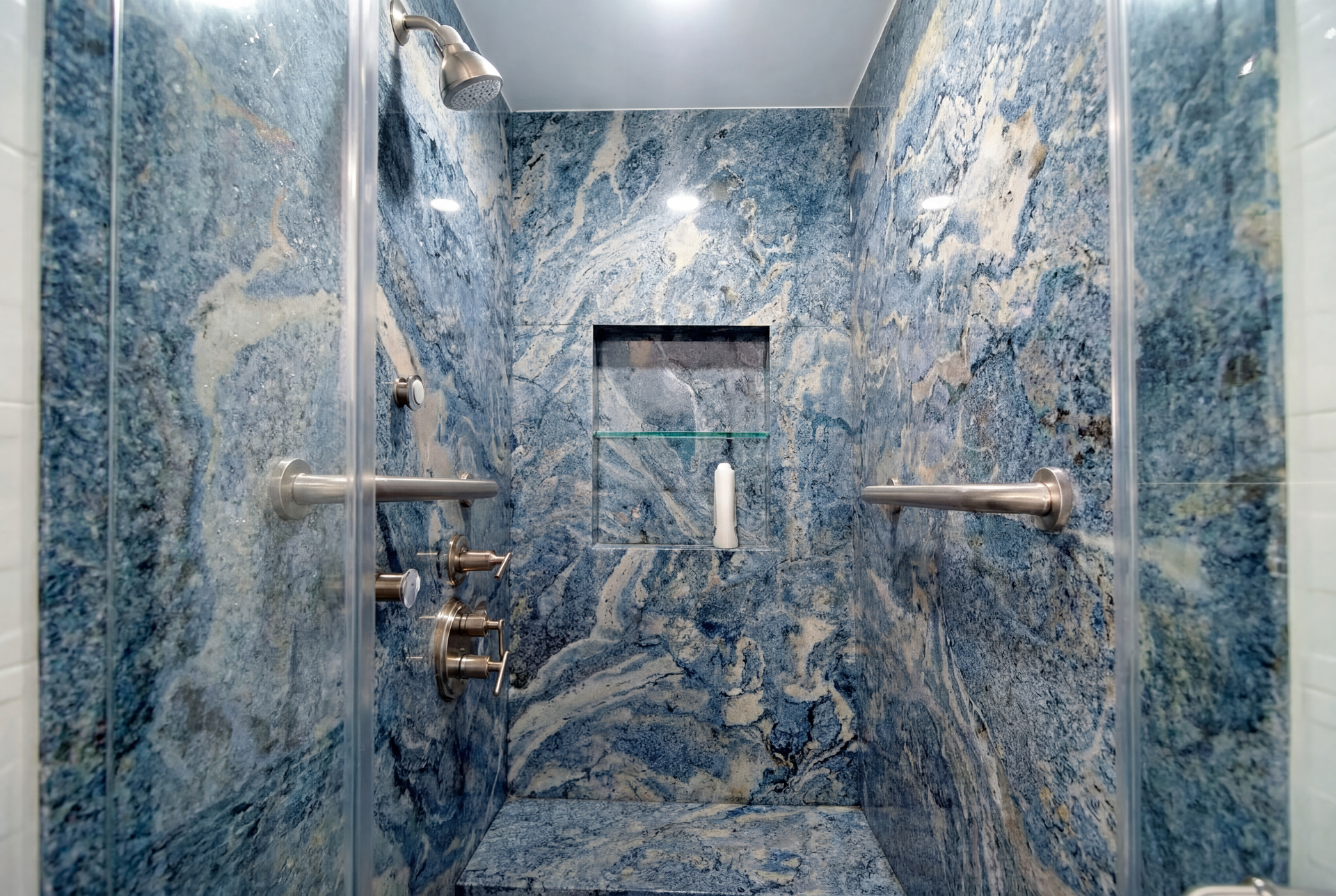 Blue and white marble-tiled shower with glass door and silver fixtures. Includes recessed shelf with shampoo bottle.