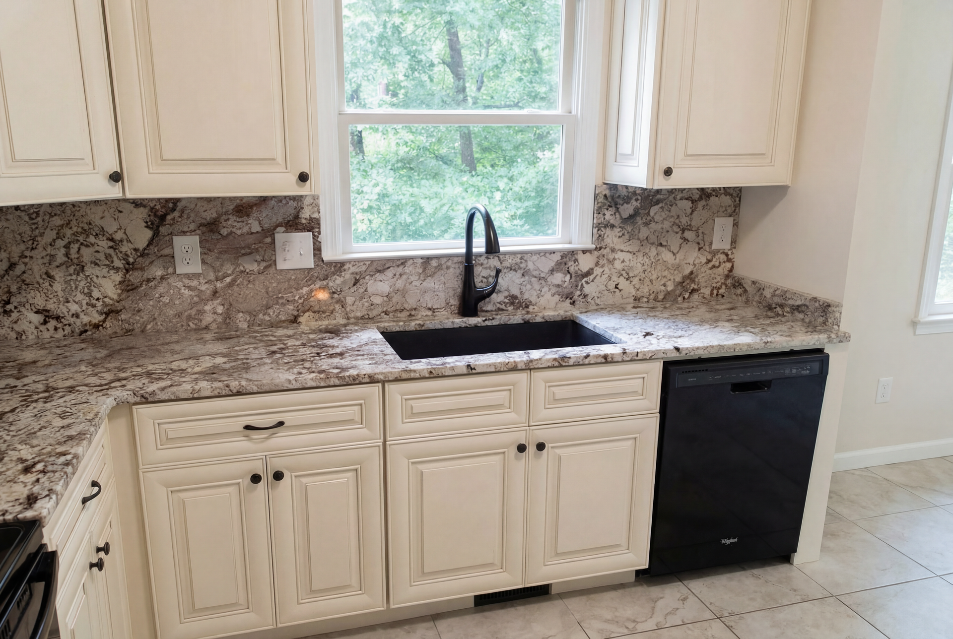 Kitchen with cream cabinets, granite countertops, black sink and faucet, and dishwasher.