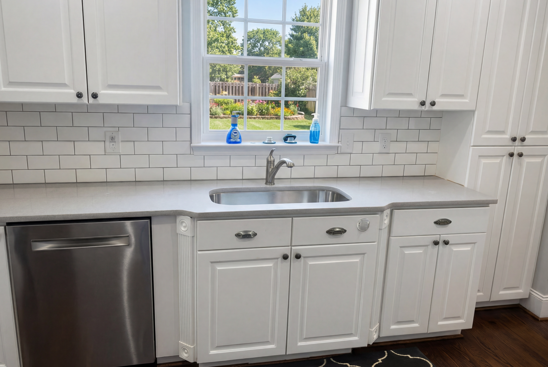 White kitchen with stainless steel appliances, sink under a window, and white cabinetry.