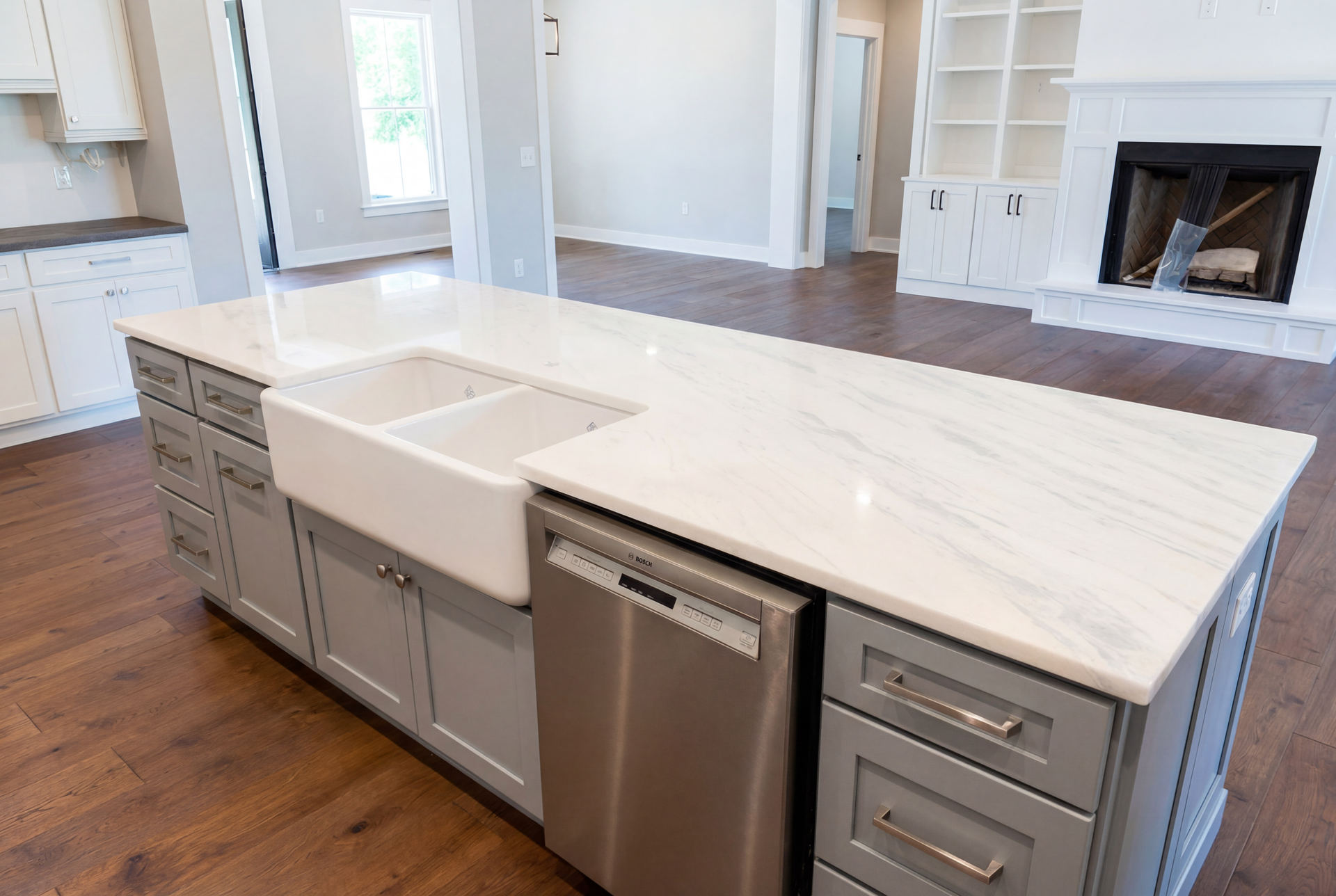 Kitchen island with white countertop, gray cabinets, farmhouse sink, and dishwasher. Hardwood floor.