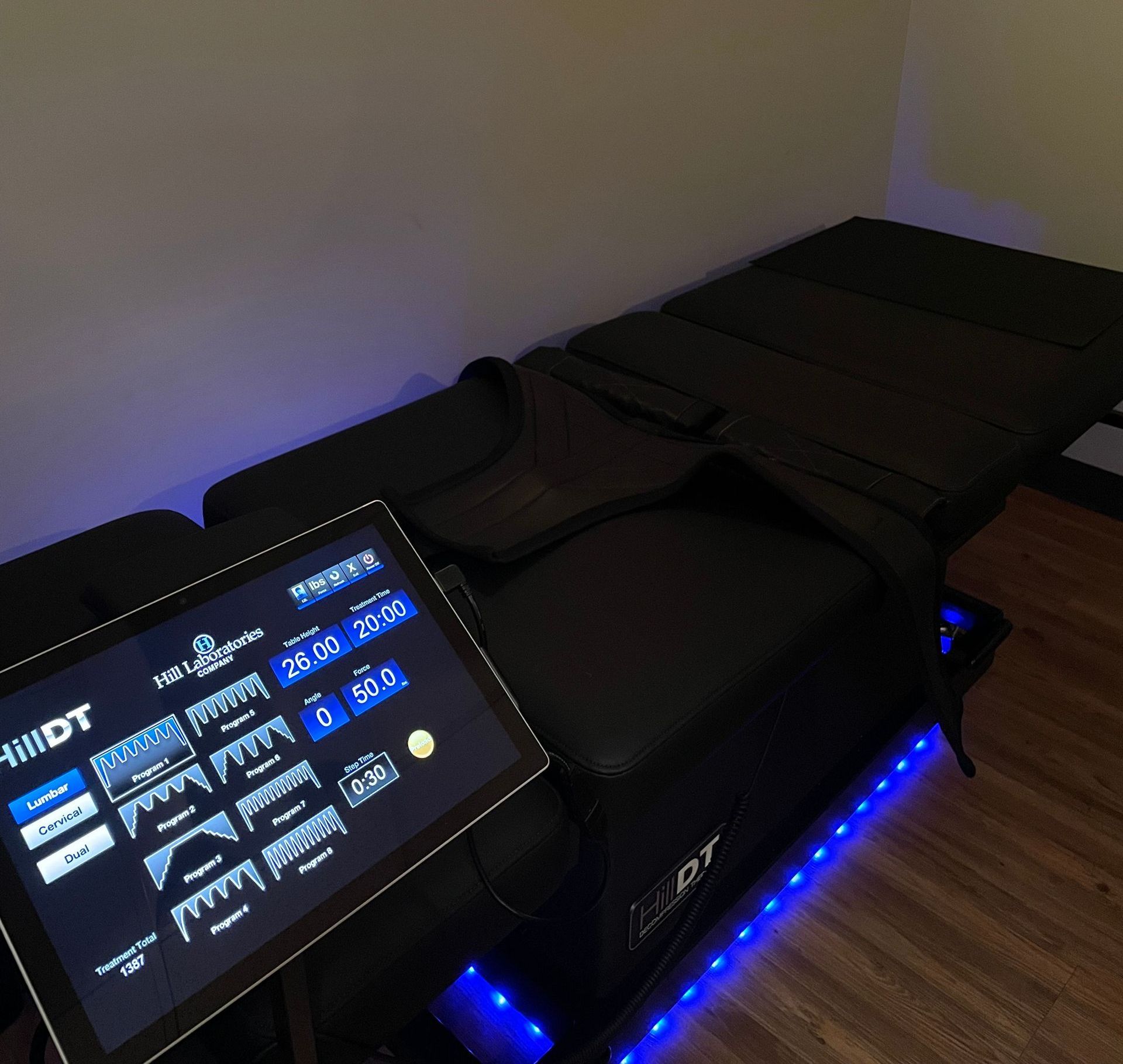 A Hill DT spinal decompression table with a digital control touchscreen, illuminated by blue floor lighting.