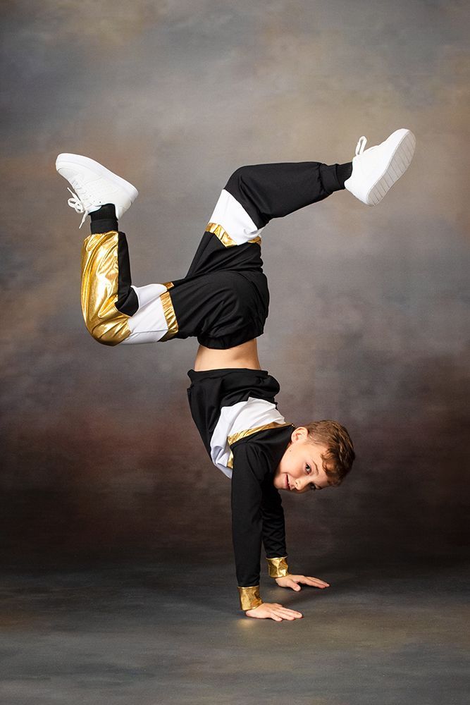 Person doing a one-handed handstand breakdance pose in black, gold, and white clothing