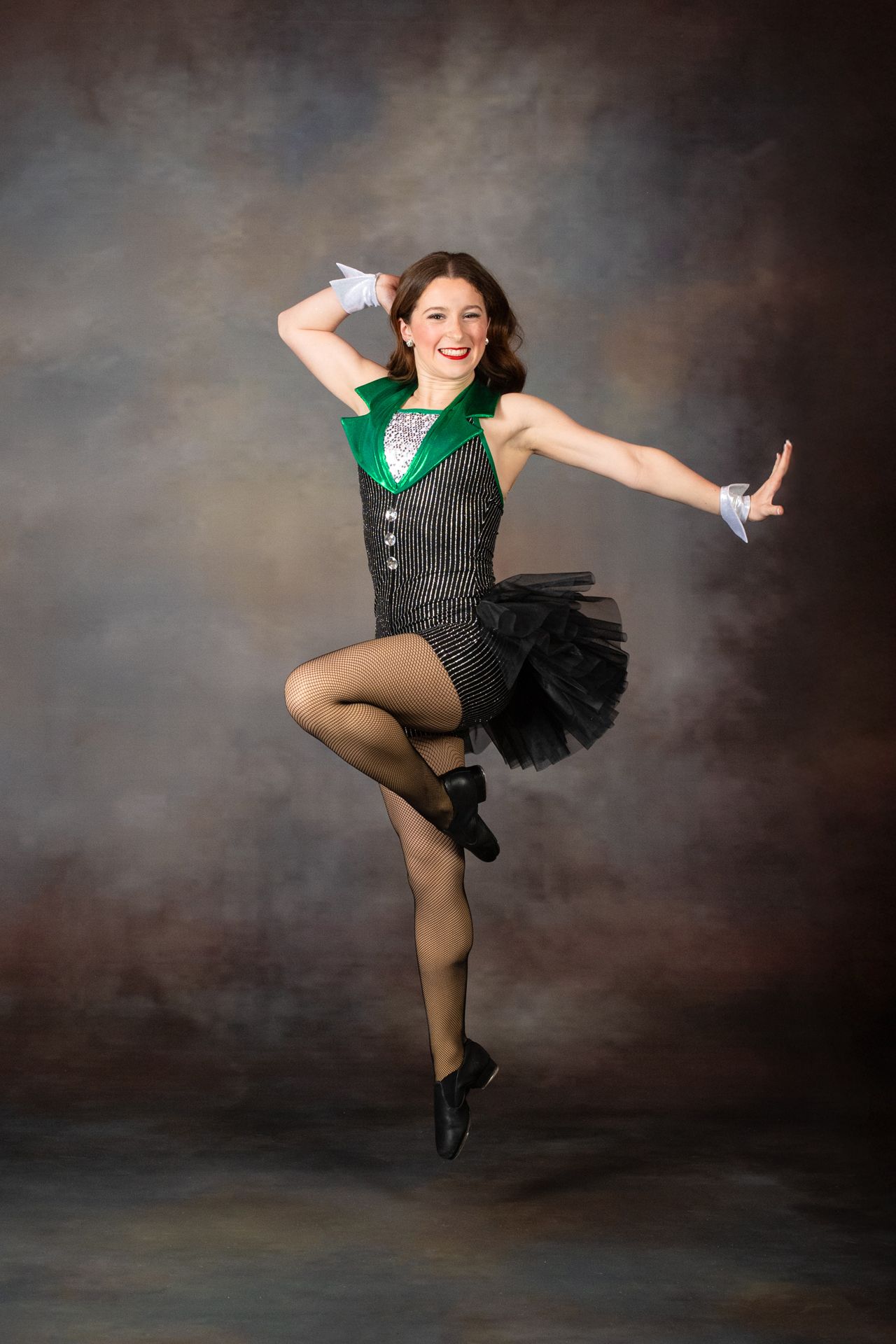 Dancer in a black and green costume striking a high-kick pose against a studio backdrop.