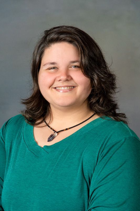 Smiling dance instructor in a teal top and black necklace against a gray background