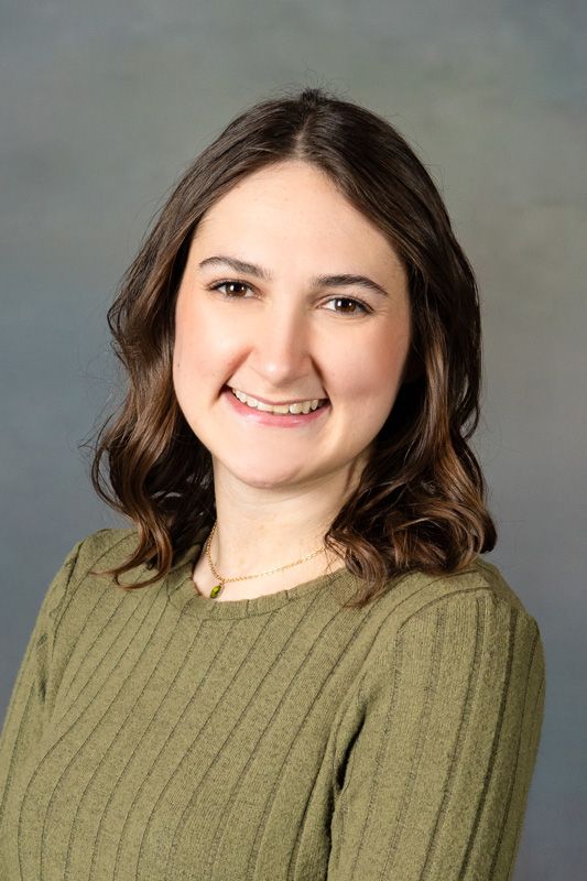 Smiling dance instructor  in an olive-green sweater against a neutral studio backdrop