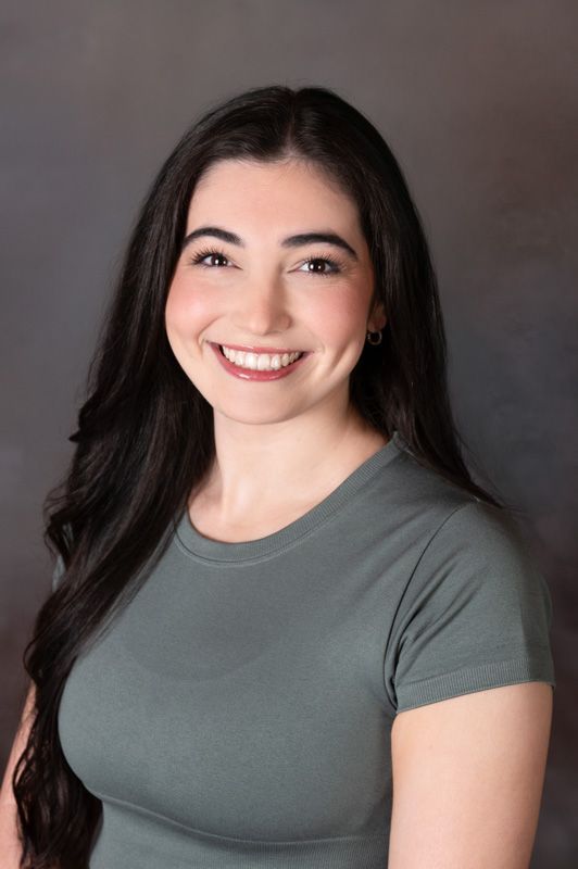 Smiling dance instructor in a gray shirt against a neutral studio backdrop