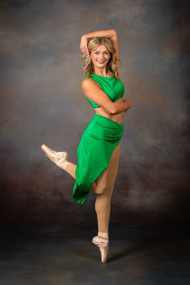 Dancer in a green costume striking a ballet pose against a dark studio backdrop