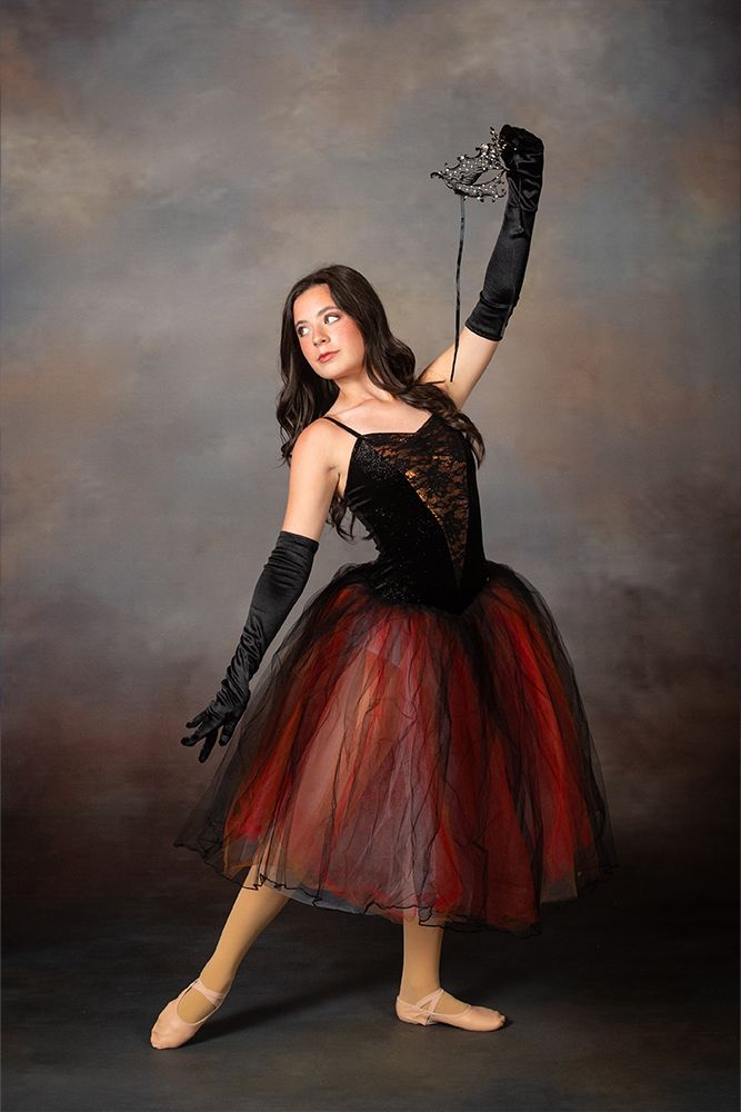 Ballet dancer in black and red costume posing against a gray studio backdrop