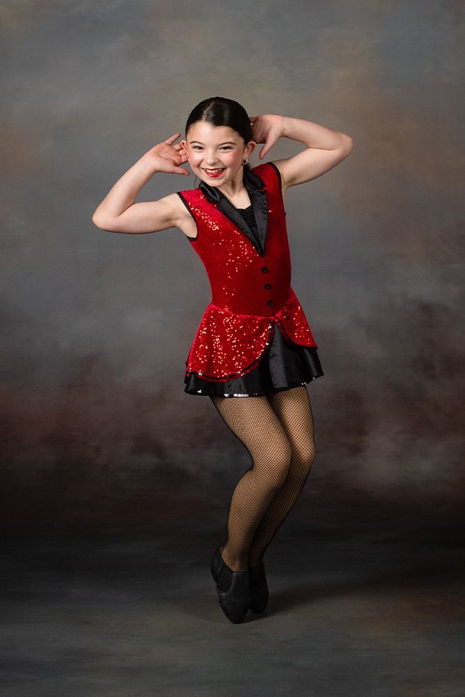 Dancer in red sequined costume posing on one leg against a gray studio backdrop