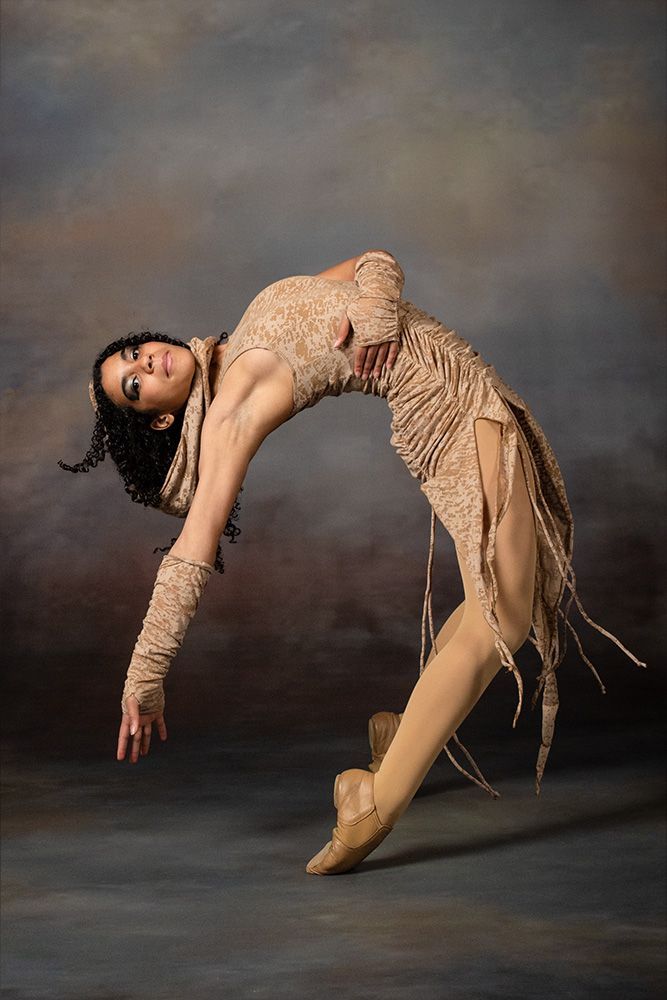 Contemporary dancer in a beige costume arching backward against a gray studio backdrop
