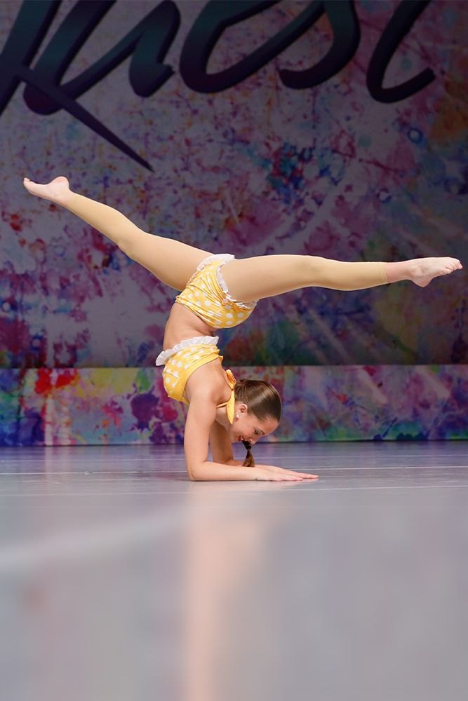 Gymnast performing a handstand split pose on a competition floor with a colorful backdrop