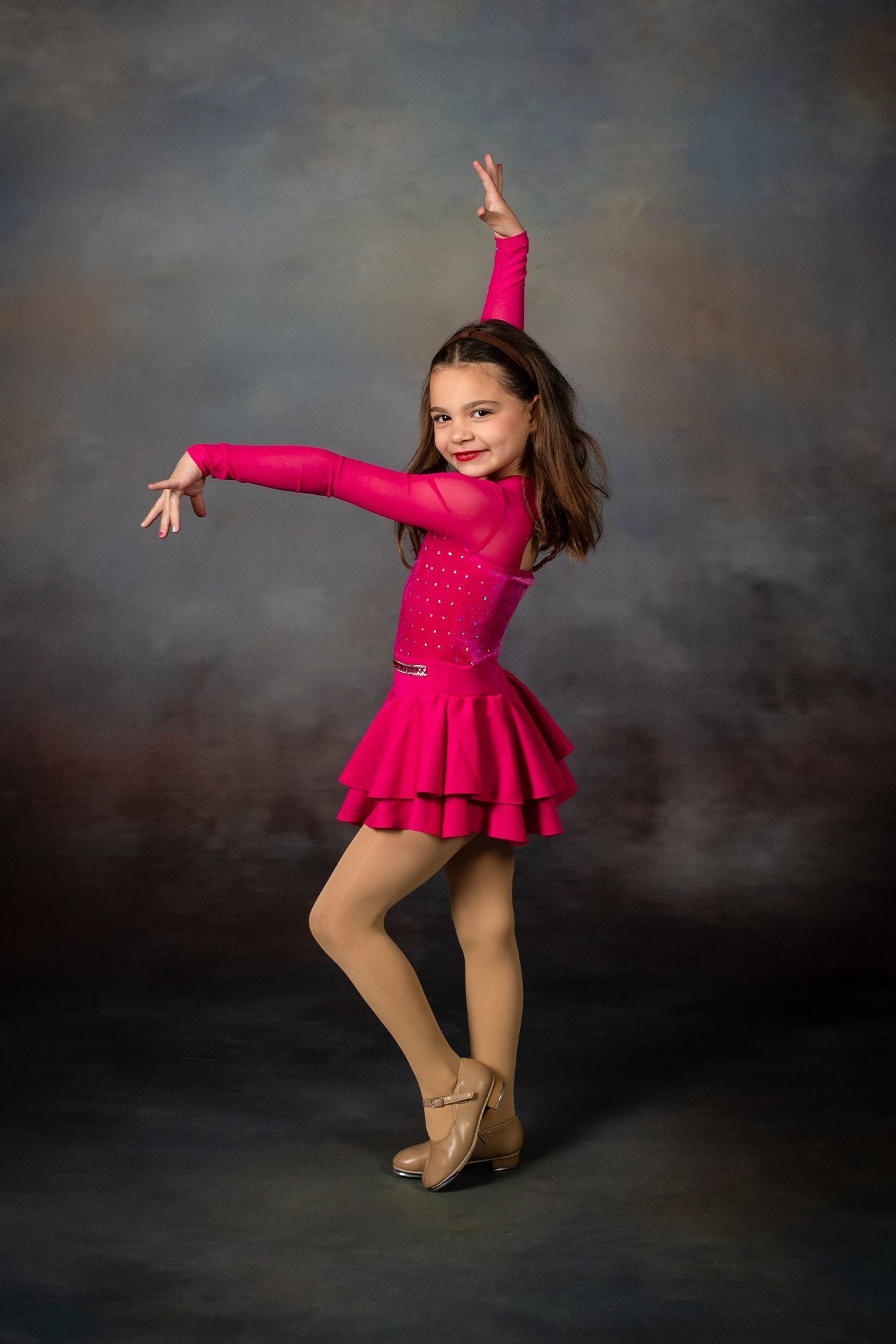 Girl in bright pink dance costume posing against a dark studio backdrop