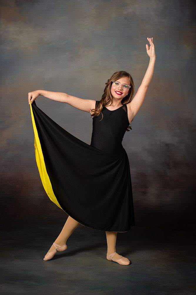 Woman posing in a black dress with a yellow hem against a dark studio backdrop