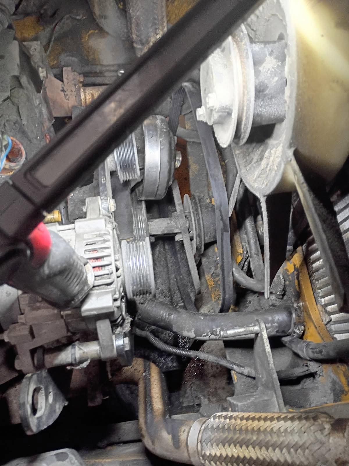 Close-up of a car engine with belts, pulleys, hoses, and metal parts visible.