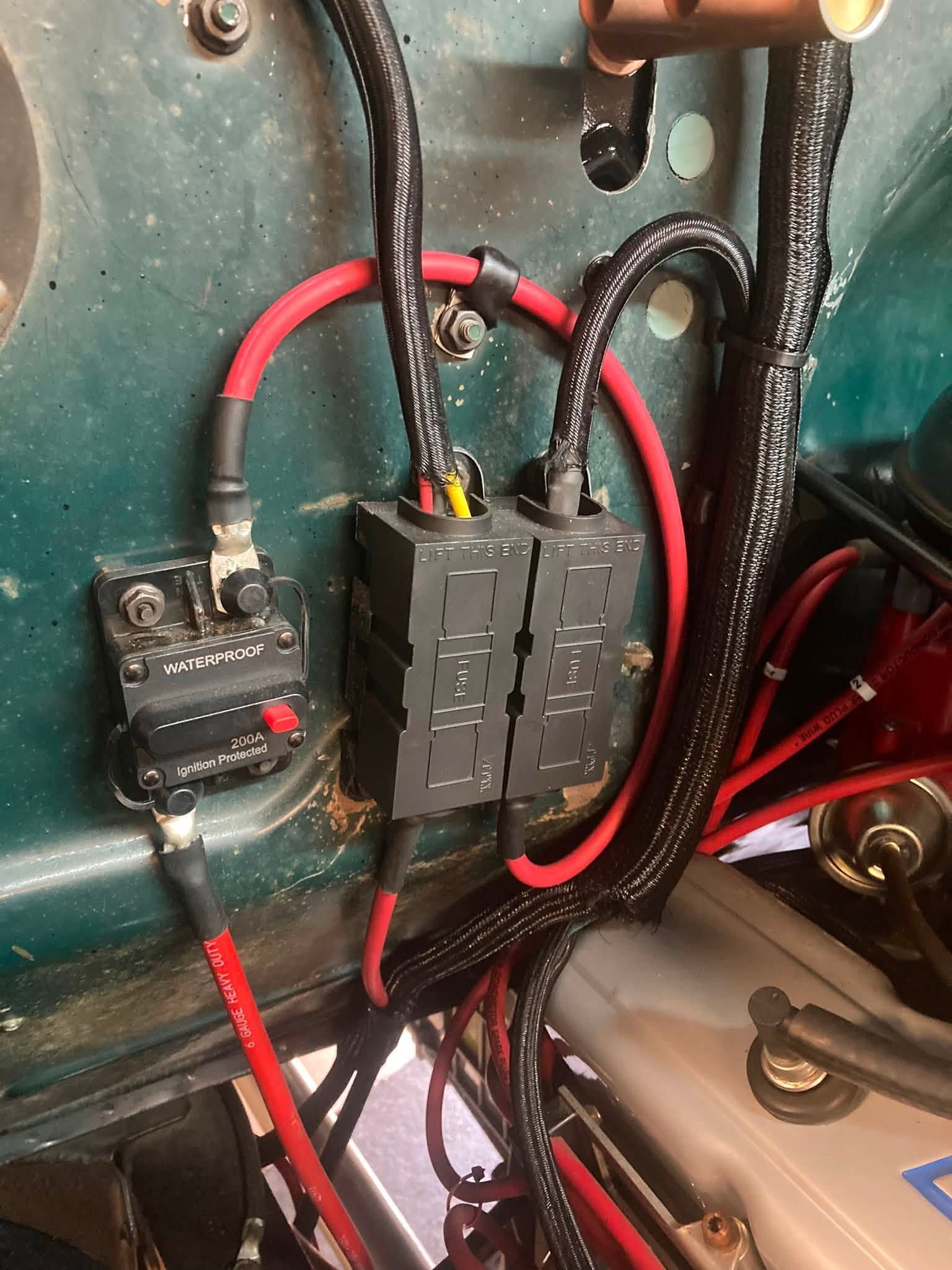 Close-up of electrical wiring, fuses, and red cables inside a vehicle panel