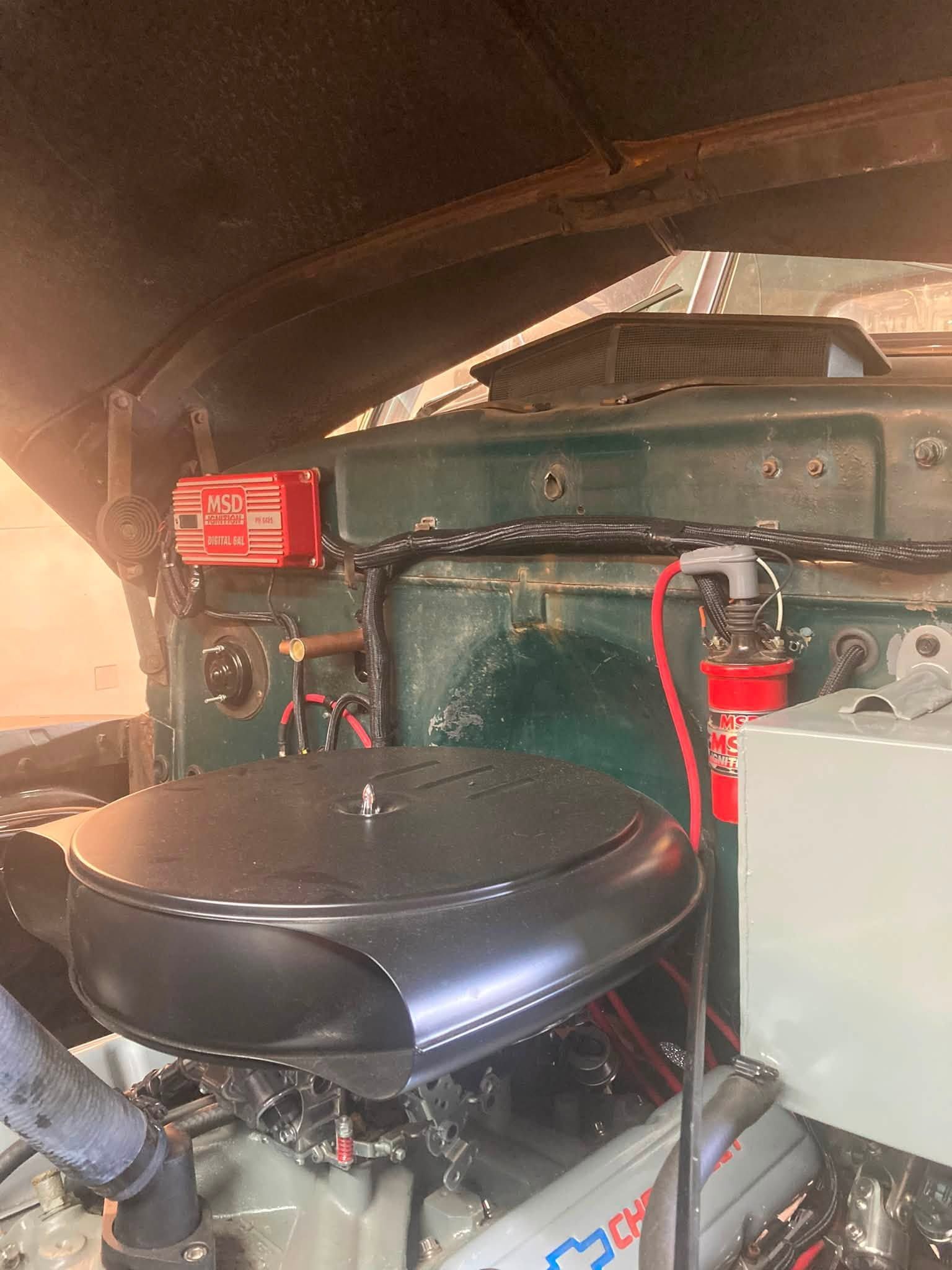 Vintage car engine bay with black seat in foreground and green body panel under warm light