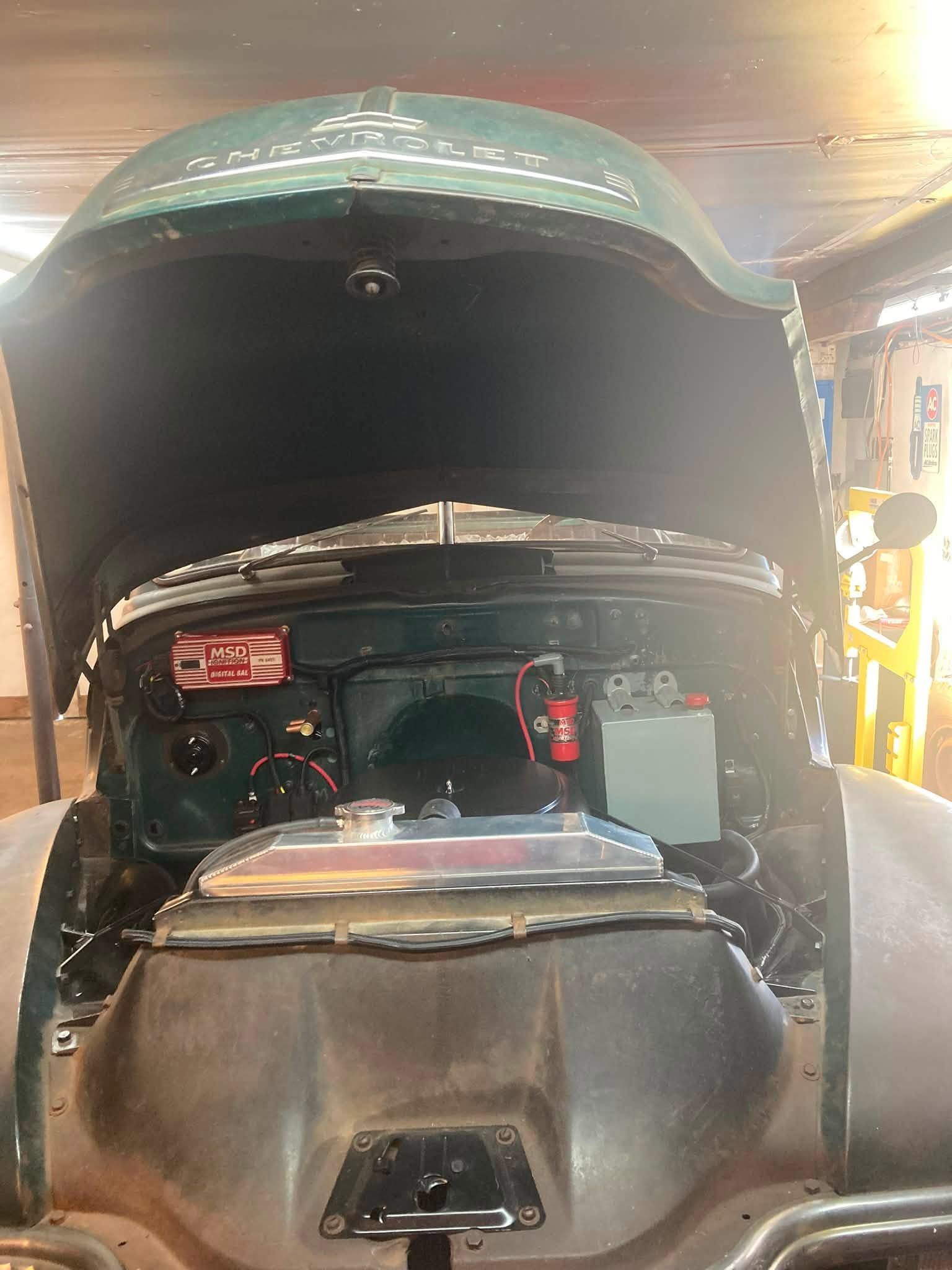 Open engine compartment of a green vehicle, showing mechanical components inside.