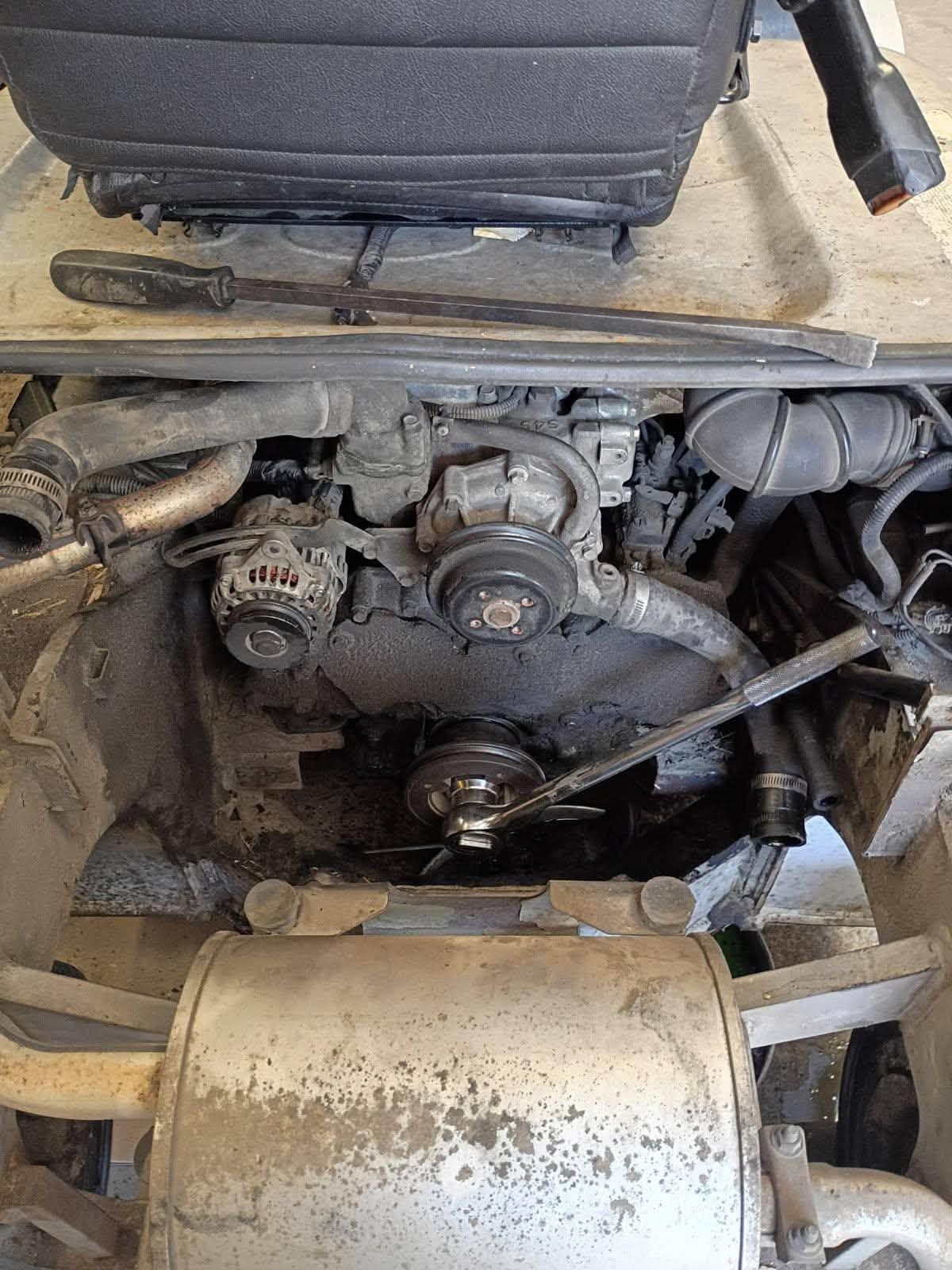 Dirty engine compartment under a vehicle, showing belts, pulleys, and a dusty engine block.