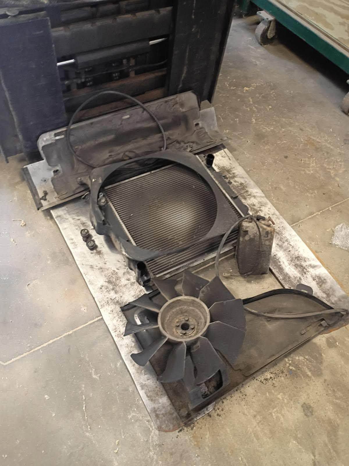 Damaged metal fan assembly lying on a dusty workshop floor, with wires and cover removed