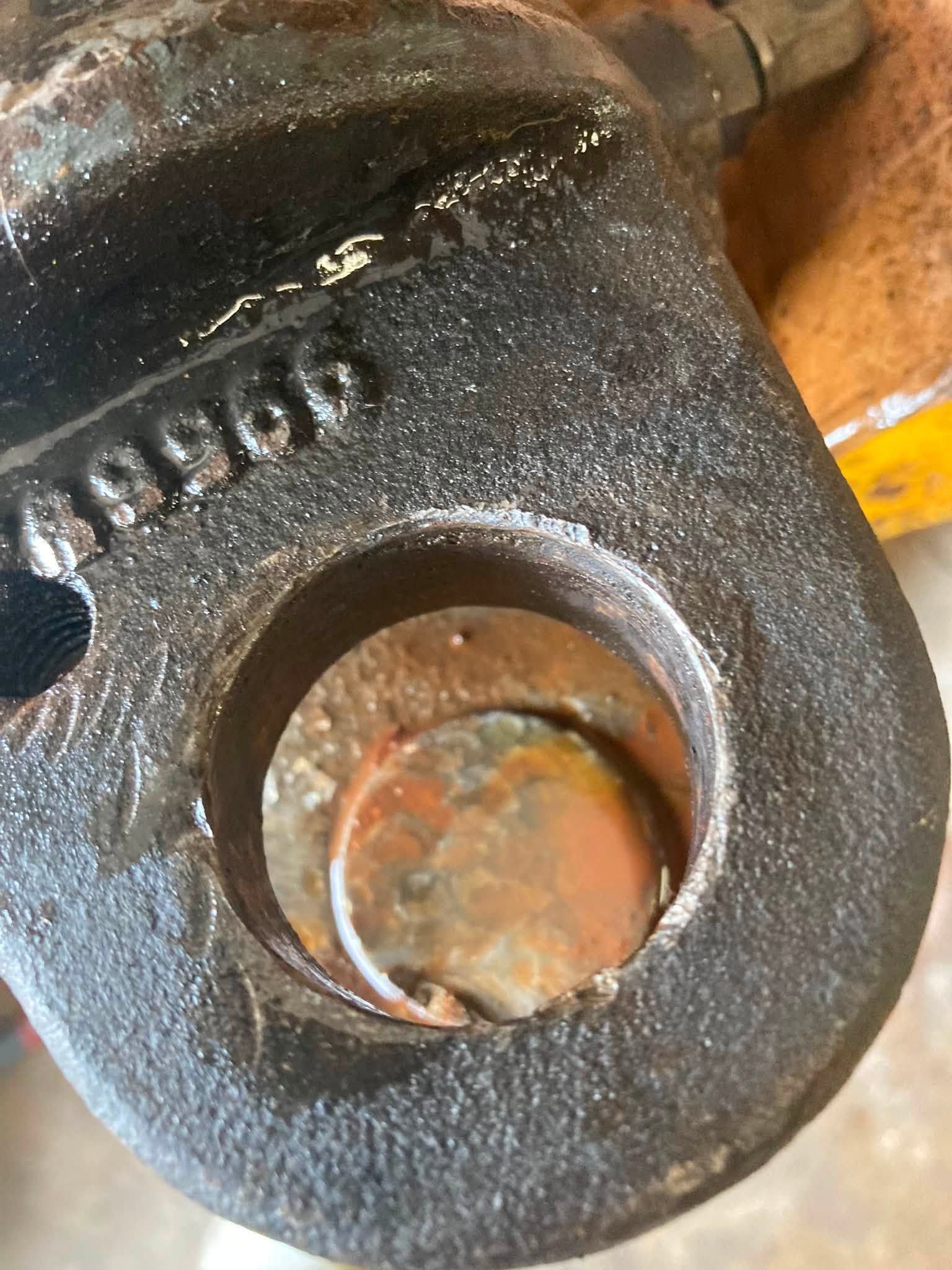 Close-up of a rusted black metal mechanical part with a circular opening and bolt hole